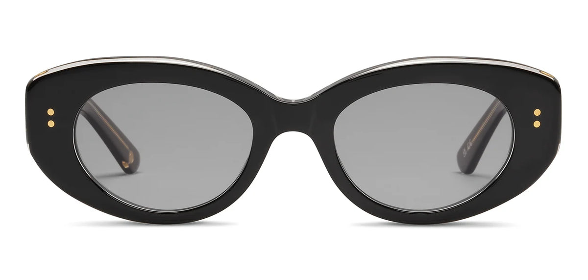 The SALT. Cass sunglasses by SALT. feature black, oval-shaped frames crafted from premium Japanese acetate with a thick design, gray lenses, and small gold dots near the hinges. Shown on a white background and viewed from the front.