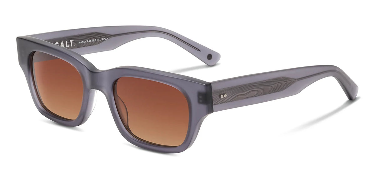 The SALT. Burnet rectangular sunglasses feature a thick, translucent gray frame crafted from premium Japanese acetate, accented by woodgrain detail on the temples and finished with brown gradient lenses that have anti-reflective coatings; they are displayed at an angle on a white background.