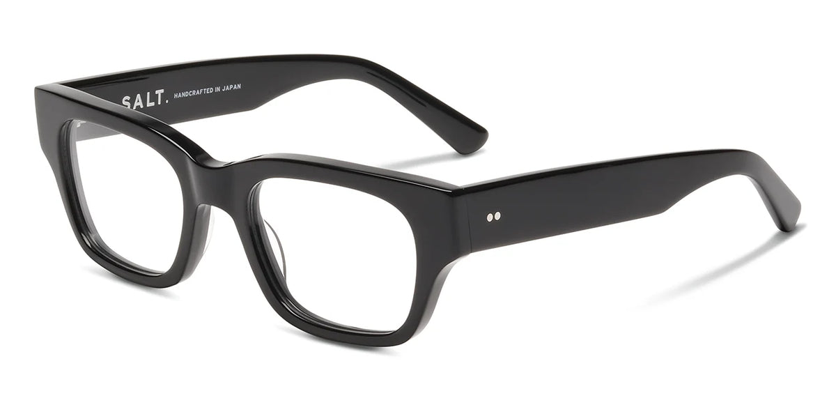 Black rectangular eyeglass frames with thick rims and arms, displayed at an angle on a white background. The SALT. Burnet optical frames by SALT. are crafted from Japanese acetate and feature the inscription “SALT. handcrafted in Japan” on the inside of the left arm.