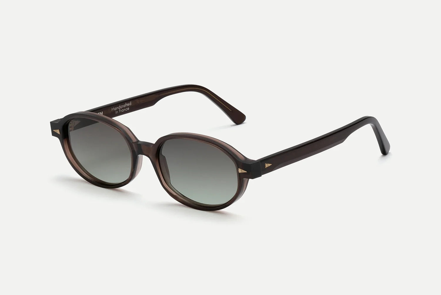 AHLEM Rohan by AHLEM are round, dark brown sunglasses handcrafted in France from premium Italian acetate. These frames have a shiny finish, feature small triangular gold accents on the front corners, and are fitted with black gradient lenses. The product is photographed against a plain white background.