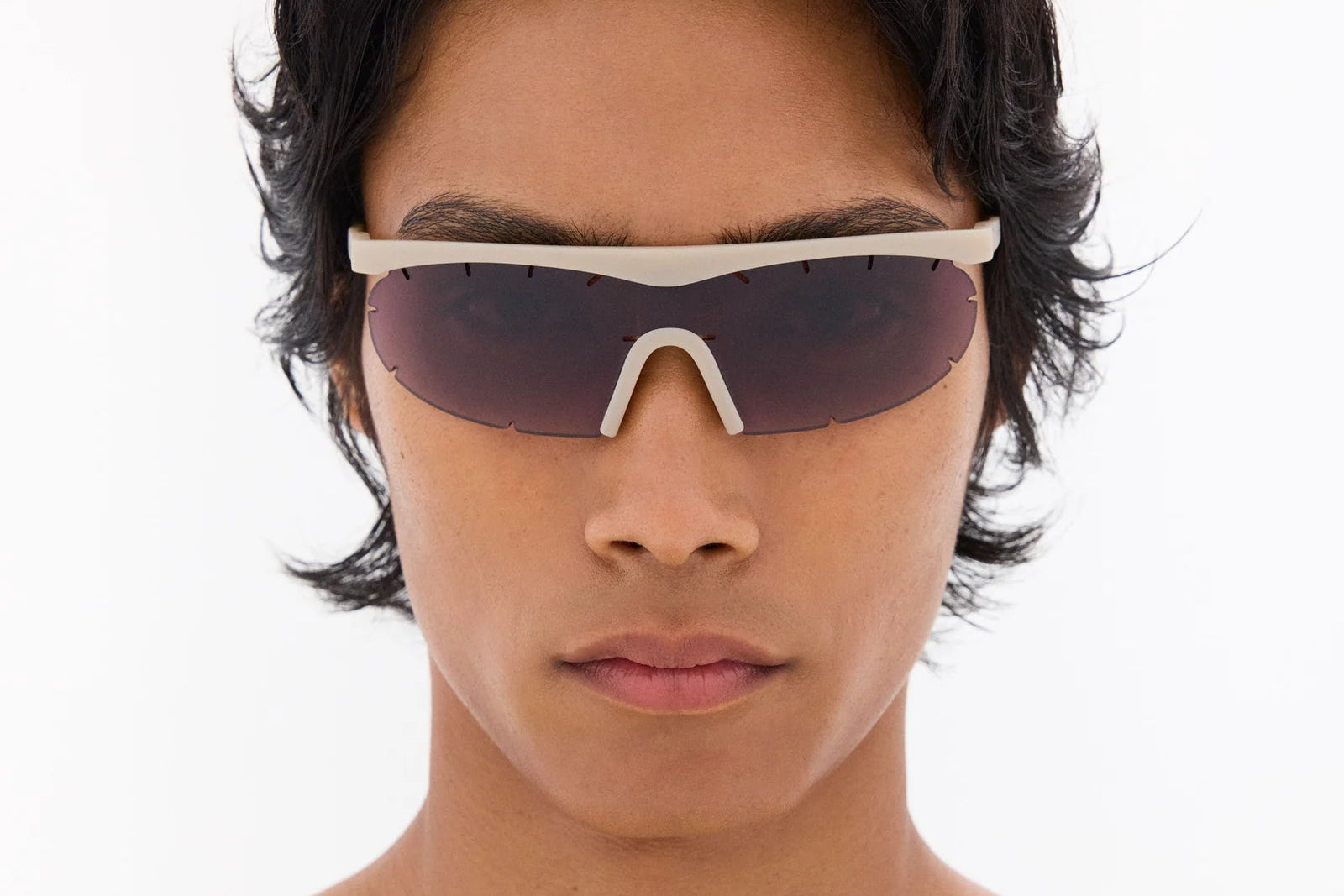 Person wearing a pair of sunglasses with a white frame on a light gray background