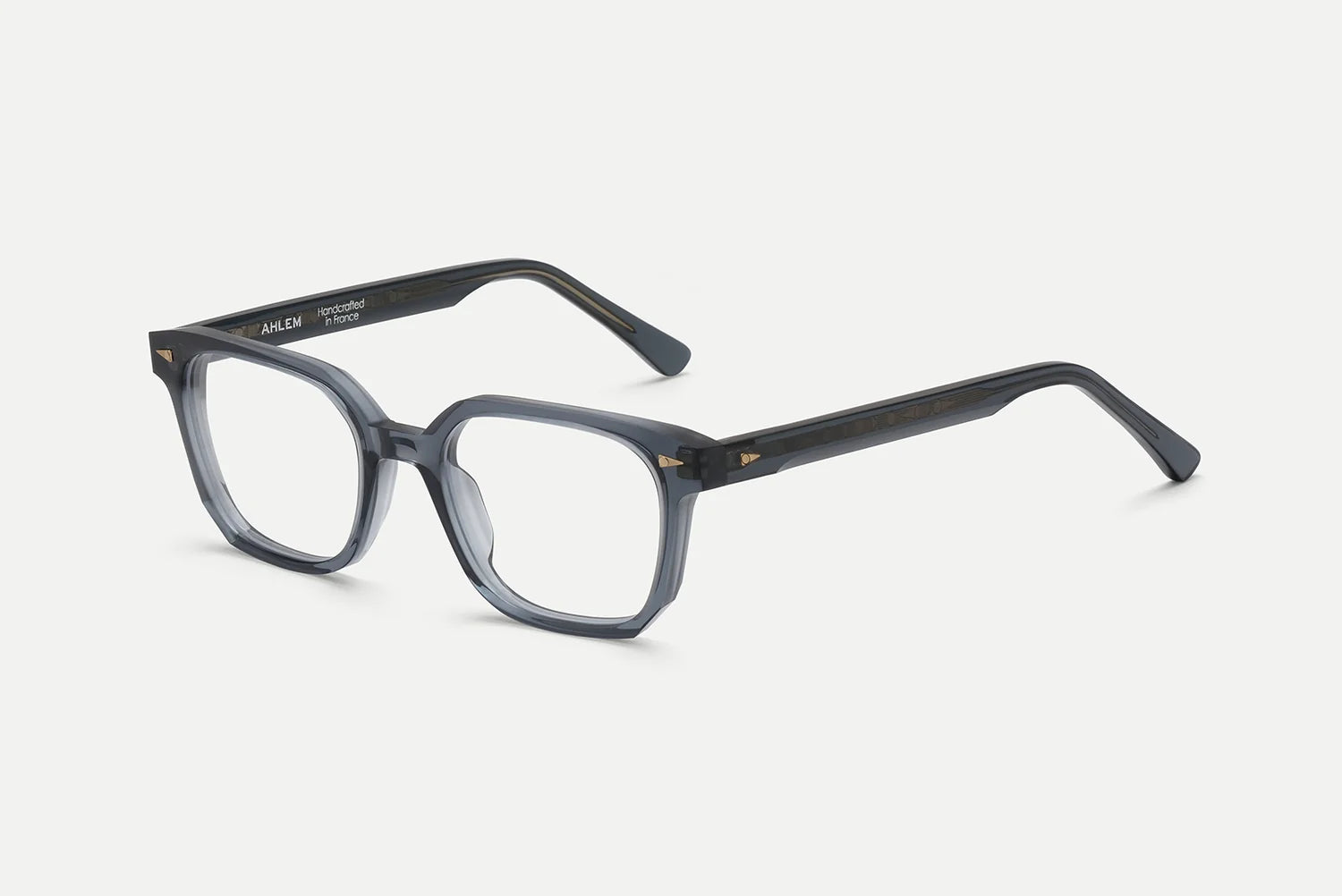 The AHLEM Houdon by AHLEM features translucent gray, square optical glasses with thick handcrafted acetate frames, angled arms, and subtle gold premium steel hardware accents at the hinges, displayed on a white background.