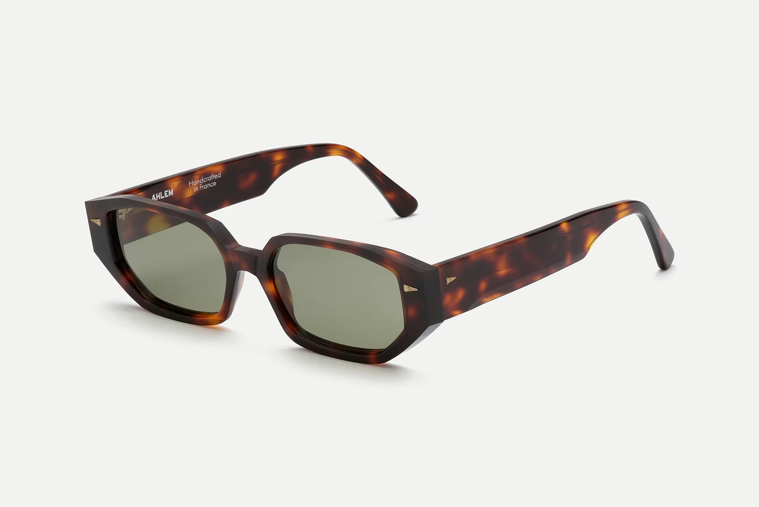The AHLEM Poitou by AHLEM showcases a tortoiseshell pattern in square frames with slightly angled edges, green-tinted lenses, thick arms, and elegant 22k gold hardware. Meticulously crafted from premium Italian acetate, these sunglasses are displayed on a plain white background.