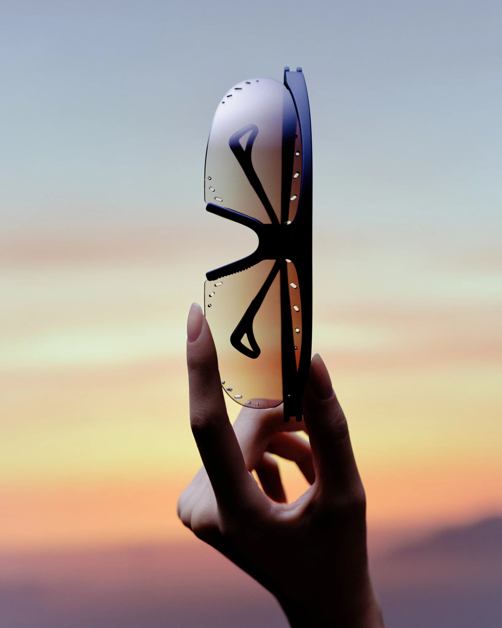 Hand holding a futuristic mask against a colorful sky