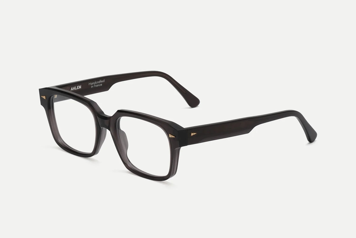 AHLEM Gros Caillou dark translucent-frame glasses handcrafted in Italian acetate, featuring rectangular lenses and gold-tone geometric rivets on the corners.