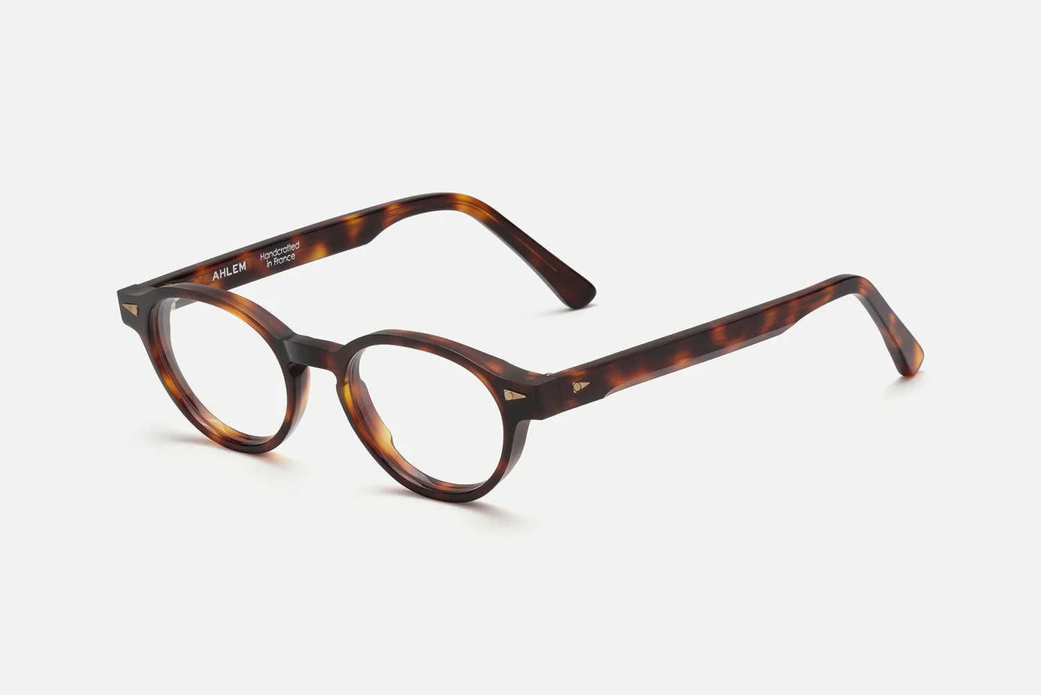 The AHLEM St Marcel eyeglasses by AHLEM, crafted in France from premium Italian acetate, feature a tortoiseshell round frame with a keyhole bridge, thick arms, and luxurious 22k gold hardware, presented on a white background.