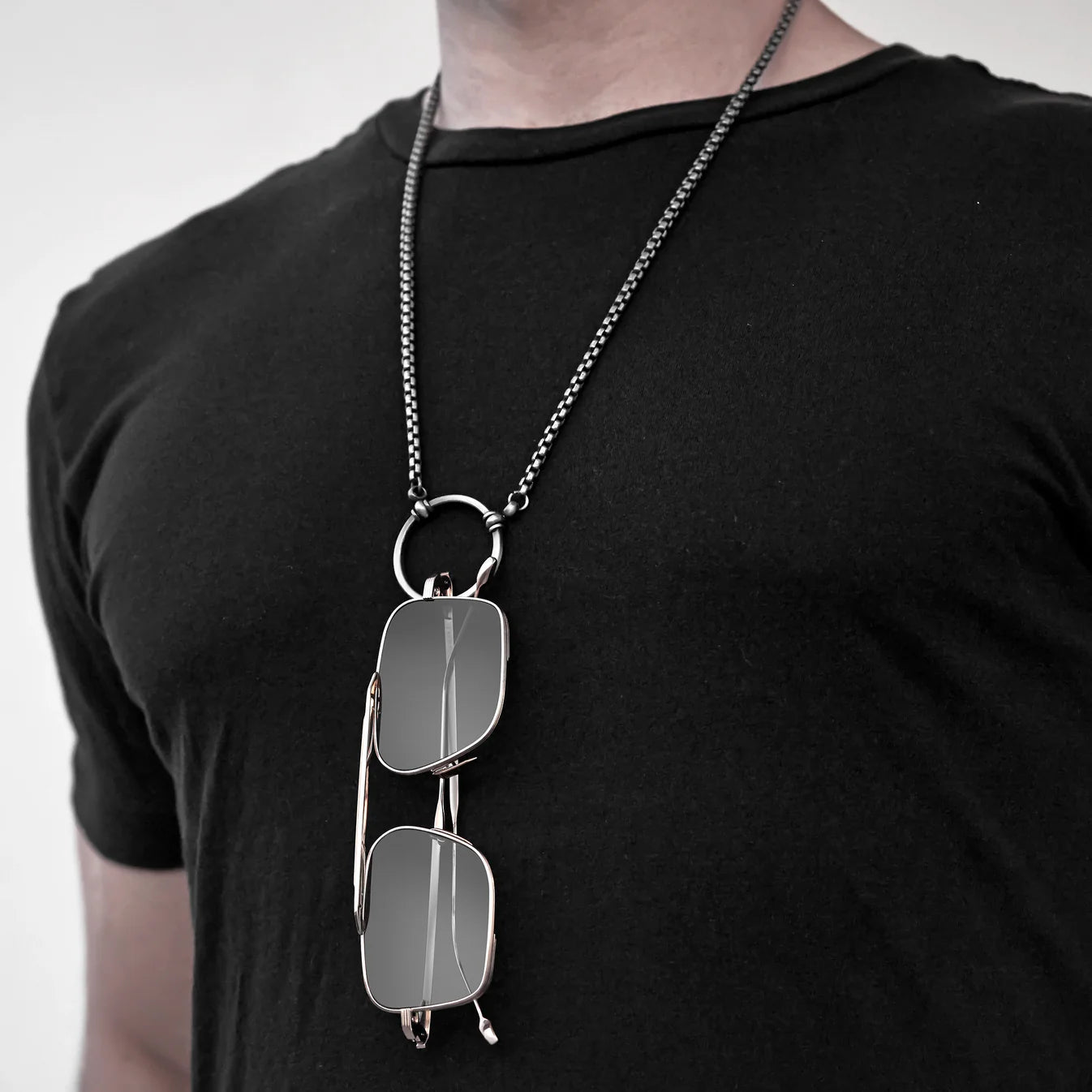 Person wearing a black t-shirt with a silver chain necklace featuring sunglasses on a plain background