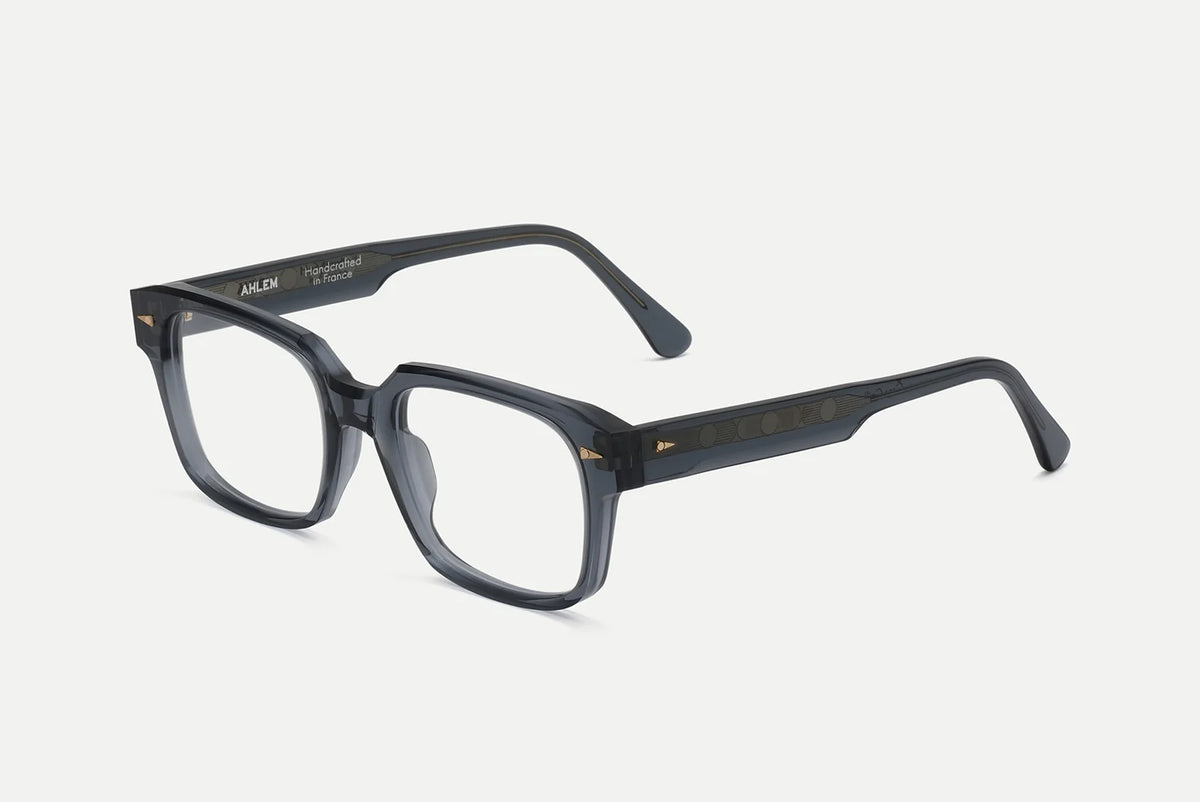 AHLEM Gros Caillou glasses in translucent grey acetate with a rectangular frame and gold arrow accents on the hinges.