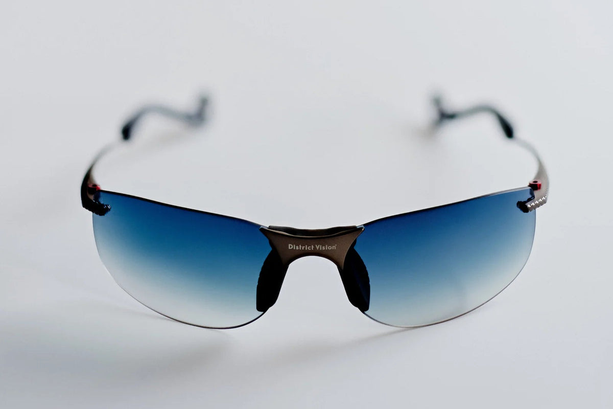 Introducing the District Vision Miho Windstream Ti by District Vision: rimless sunglasses featuring blue gradient lenses and slender black frames, designed for a customizable fit to ensure maximum comfort, elegantly displayed on a white surface.