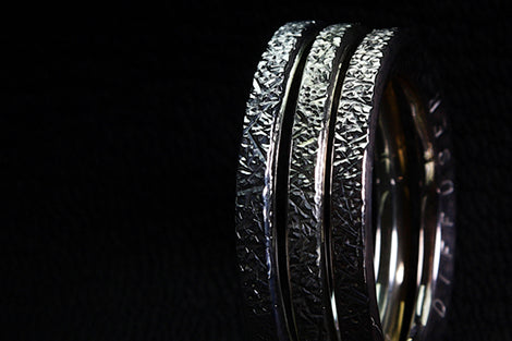 Close-up of three silver rings with textured designs on a black background