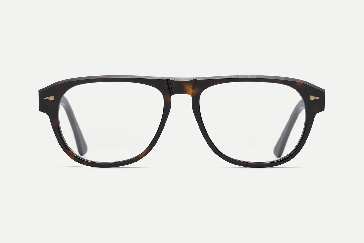 A pair of thick-framed eyeglasses with a dark brown and black tortoiseshell pattern, clear lenses, and small gold geometric accents on the temples, shown against a light gray background.