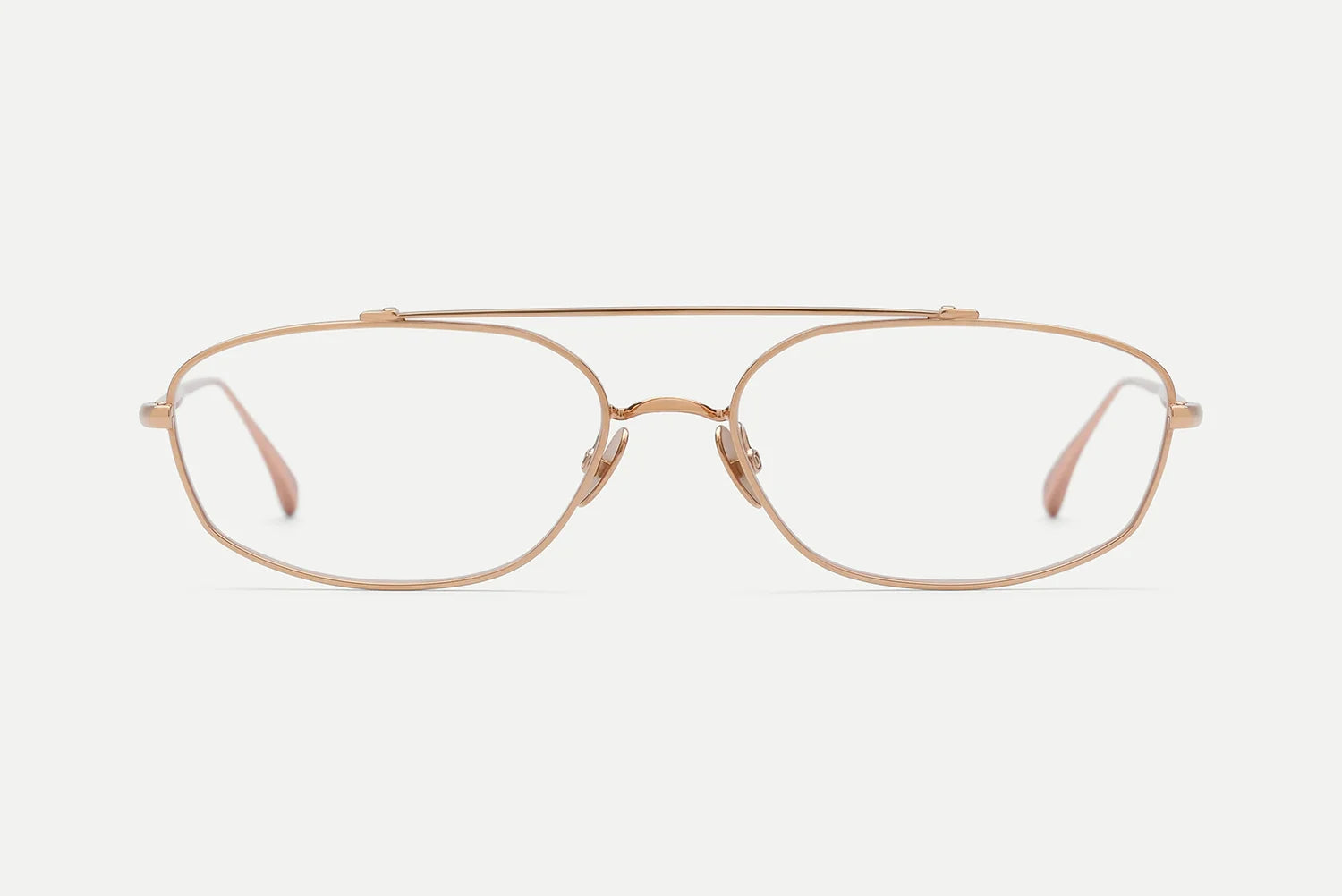 A pair of slim, oval-shaped eyeglasses with a thin rose gold metal frame and clear lenses, shown against a plain light gray background.