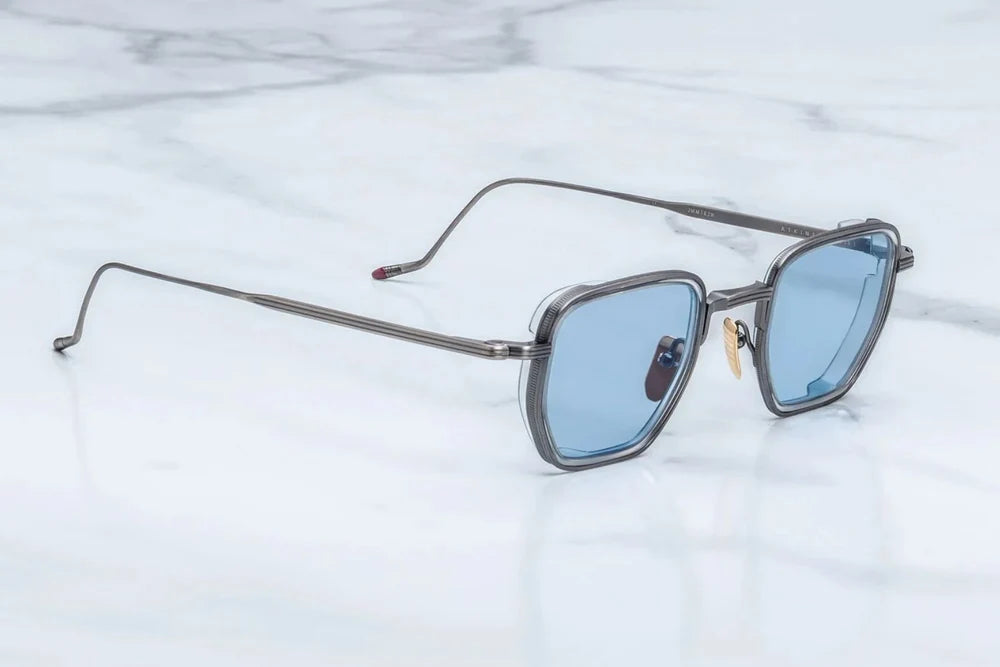 Square metal-framed sunglasses with light blue lenses resting on a white marble surface.