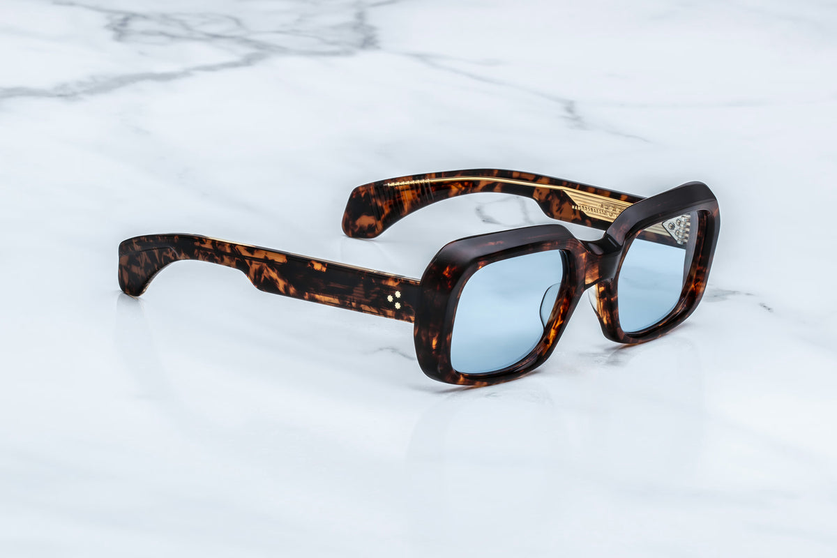 Jacques Marie Mage Aldo sunglasses by Jacques Marie Mage, crafted with exquisite craftsmanship in a brown tortoiseshell square frame and fitted with blue-tinted lenses, rest elegantly on a white marble surface.
