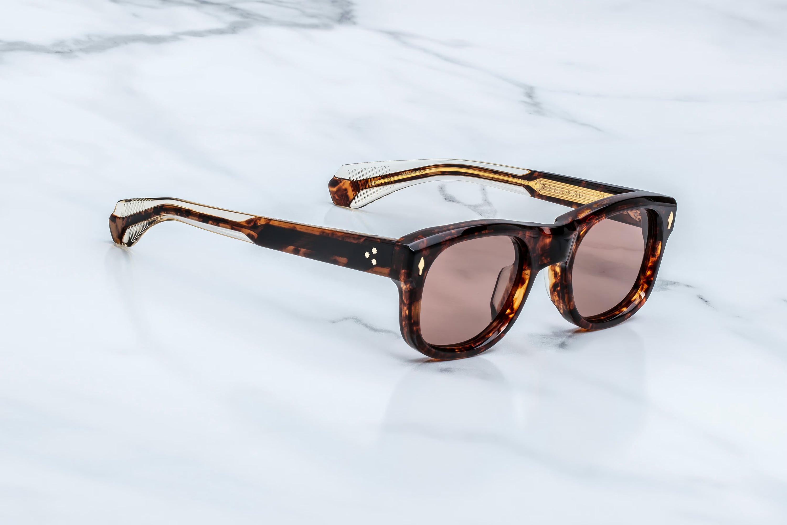 Tortoiseshell acetate sunglasses with brown lenses, resting on a white marble surface.