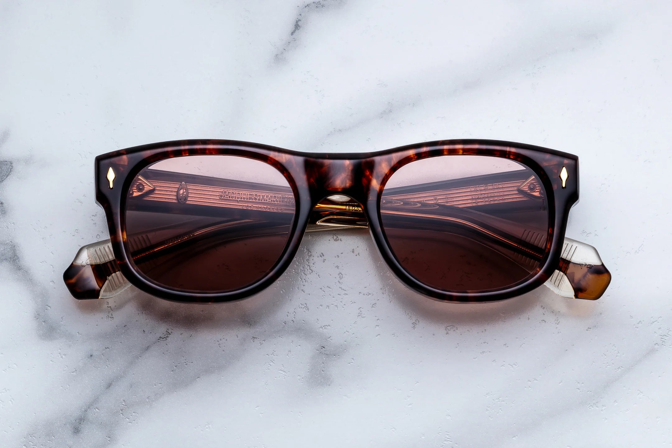 A pair of classic Wayfarer-style sunglasses with a dark tortoiseshell frame and brown lenses, resting on a white marble surface.