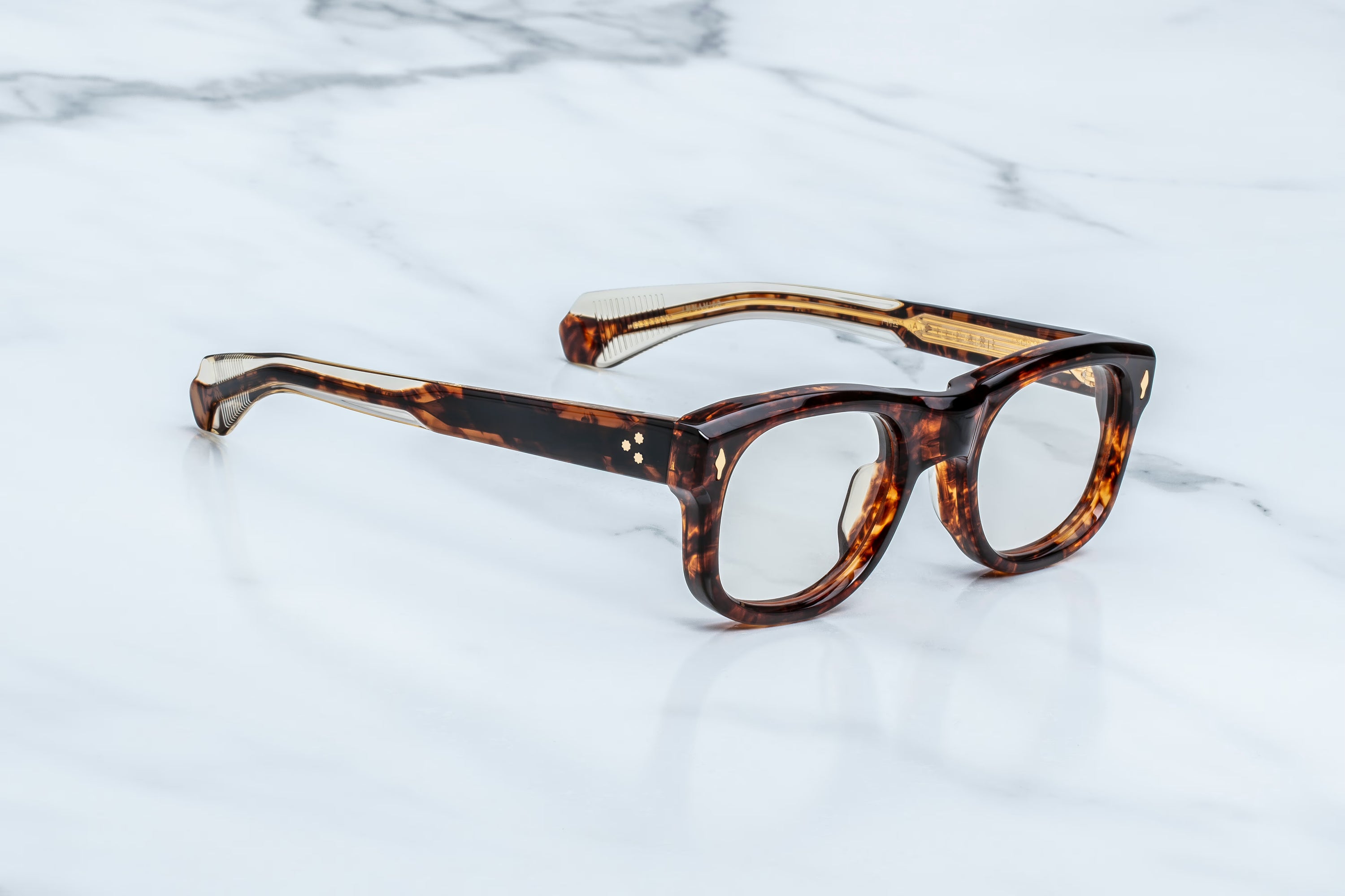 A pair of round-frame eyeglasses with a glossy tortoiseshell pattern in brown and black, resting on a white marble surface.