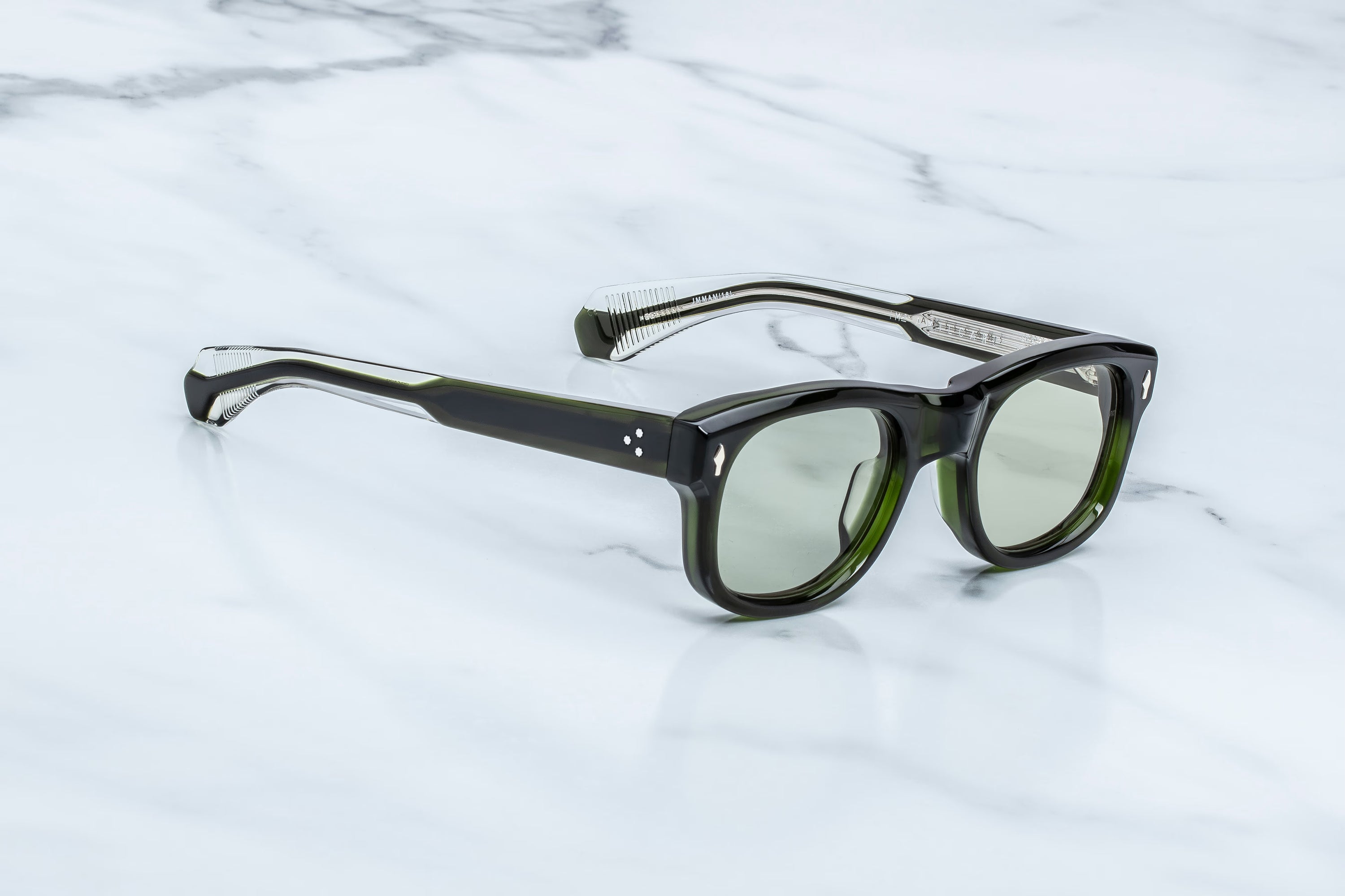 A pair of square-frame eyeglasses with translucent dark green and black frames and light green lenses, resting on a white marble surface.