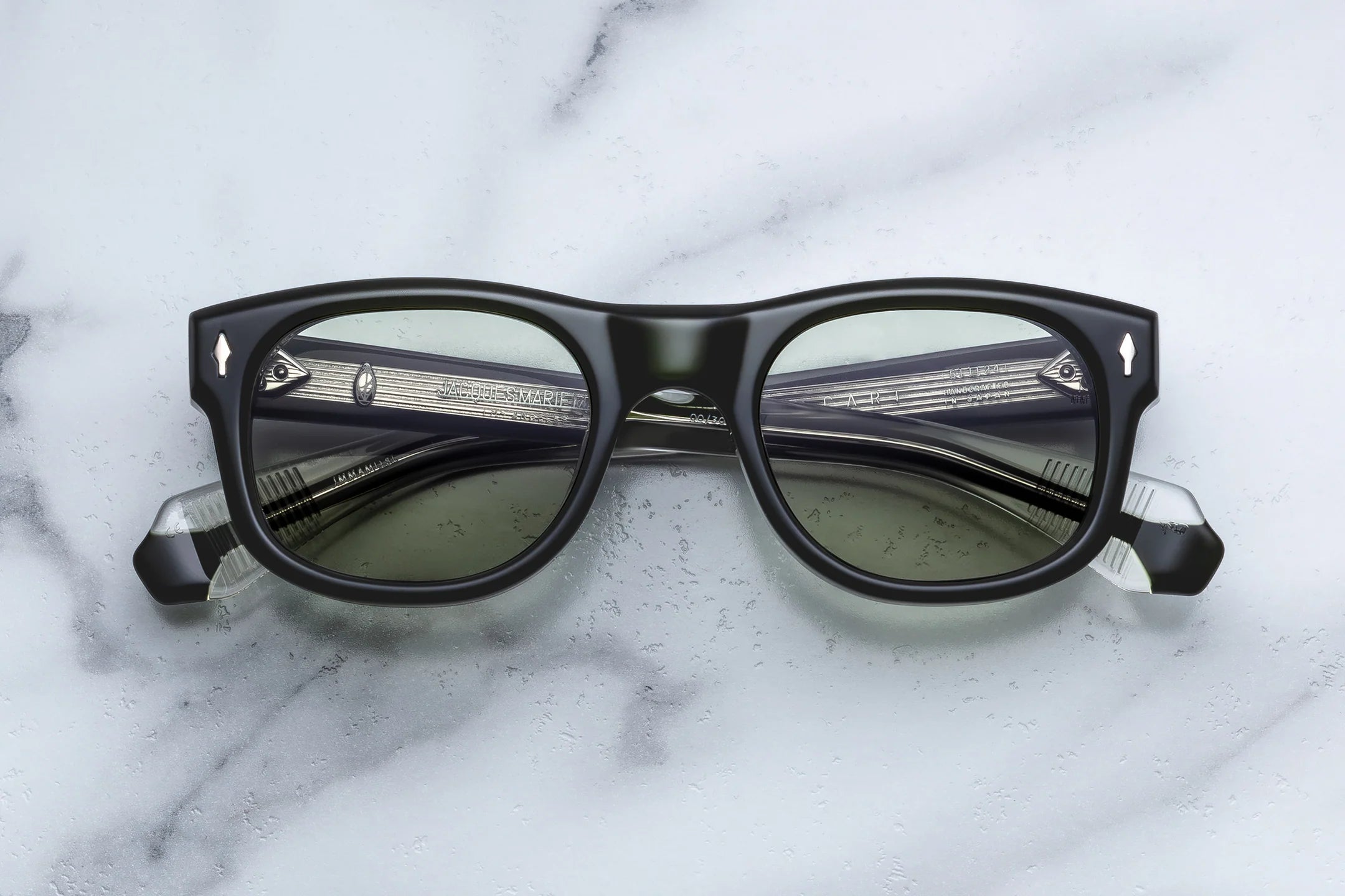 Black rectangular sunglasses with dark tinted lenses and clear acetate temples, displayed on a white marble surface.