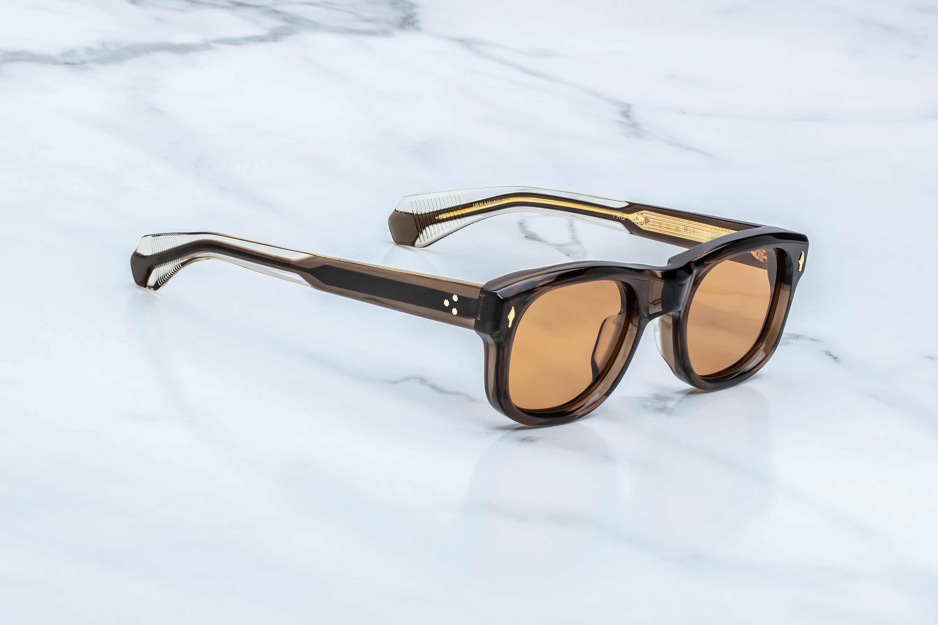 A pair of square-frame sunglasses with translucent dark brown and black frames and warm amber lenses, resting on a white marble surface.
