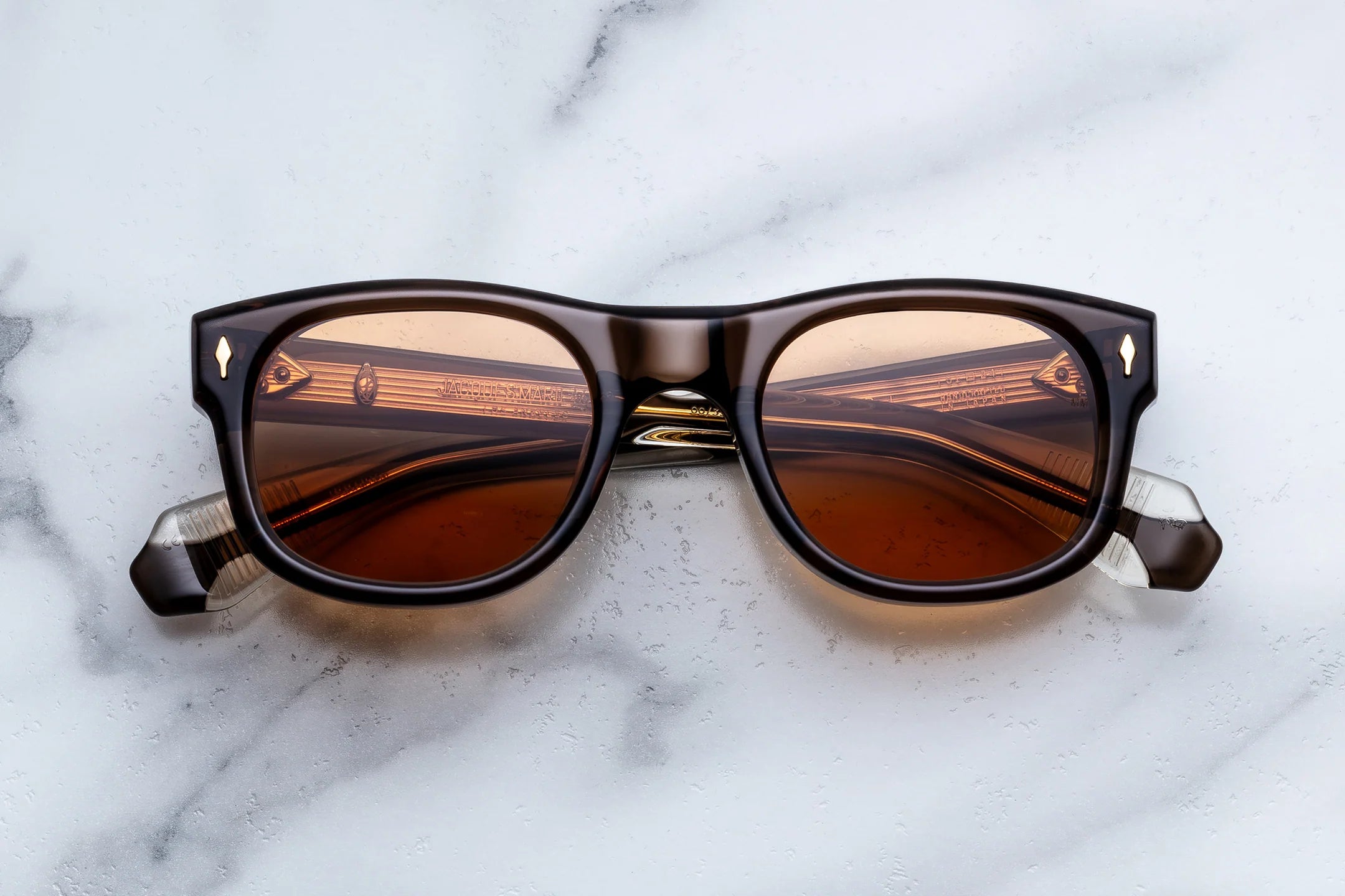 A pair of square-frame sunglasses with a dark brown translucent acetate frame and warm brown-tinted lenses, resting on a white marble surface.