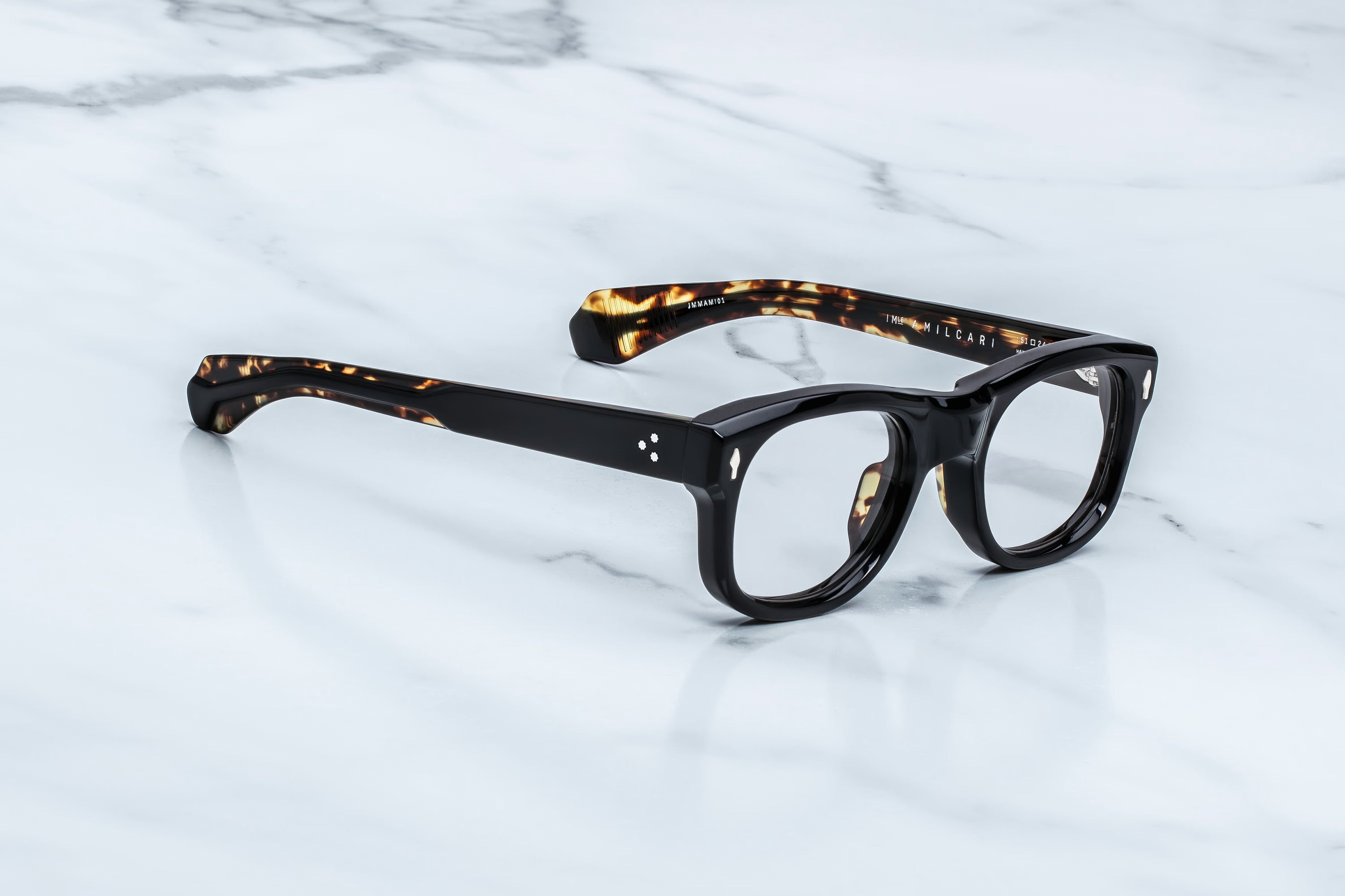 Black acetate eyeglasses with tortoiseshell-patterned temples, resting on a white marble surface.