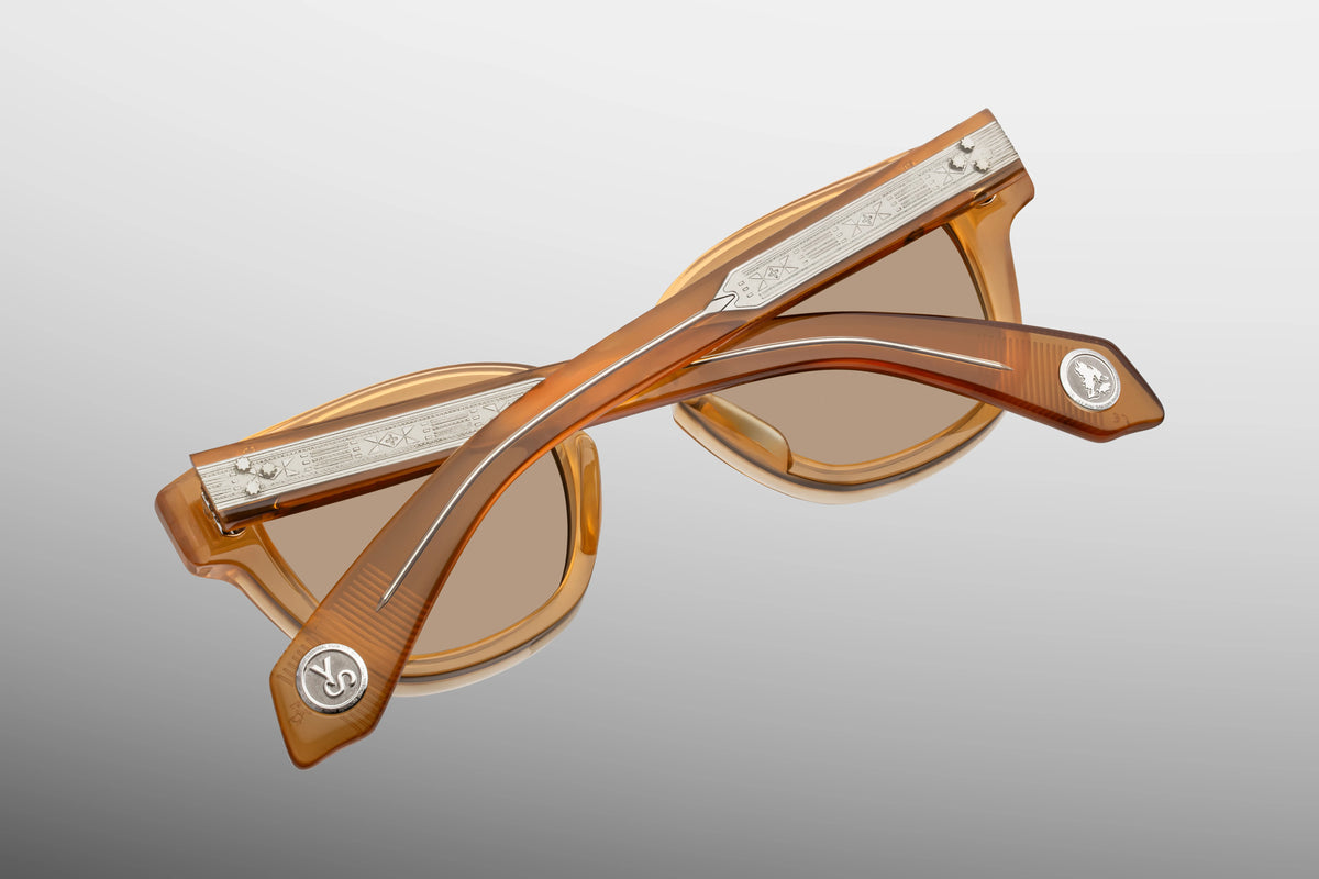 Jacques Marie Mage Yellowstone VII: Barronette In Brush sunglasses in translucent amber, featuring silver-toned engraved metal temples, decorative side emblems, and polarized mineral glass lenses.