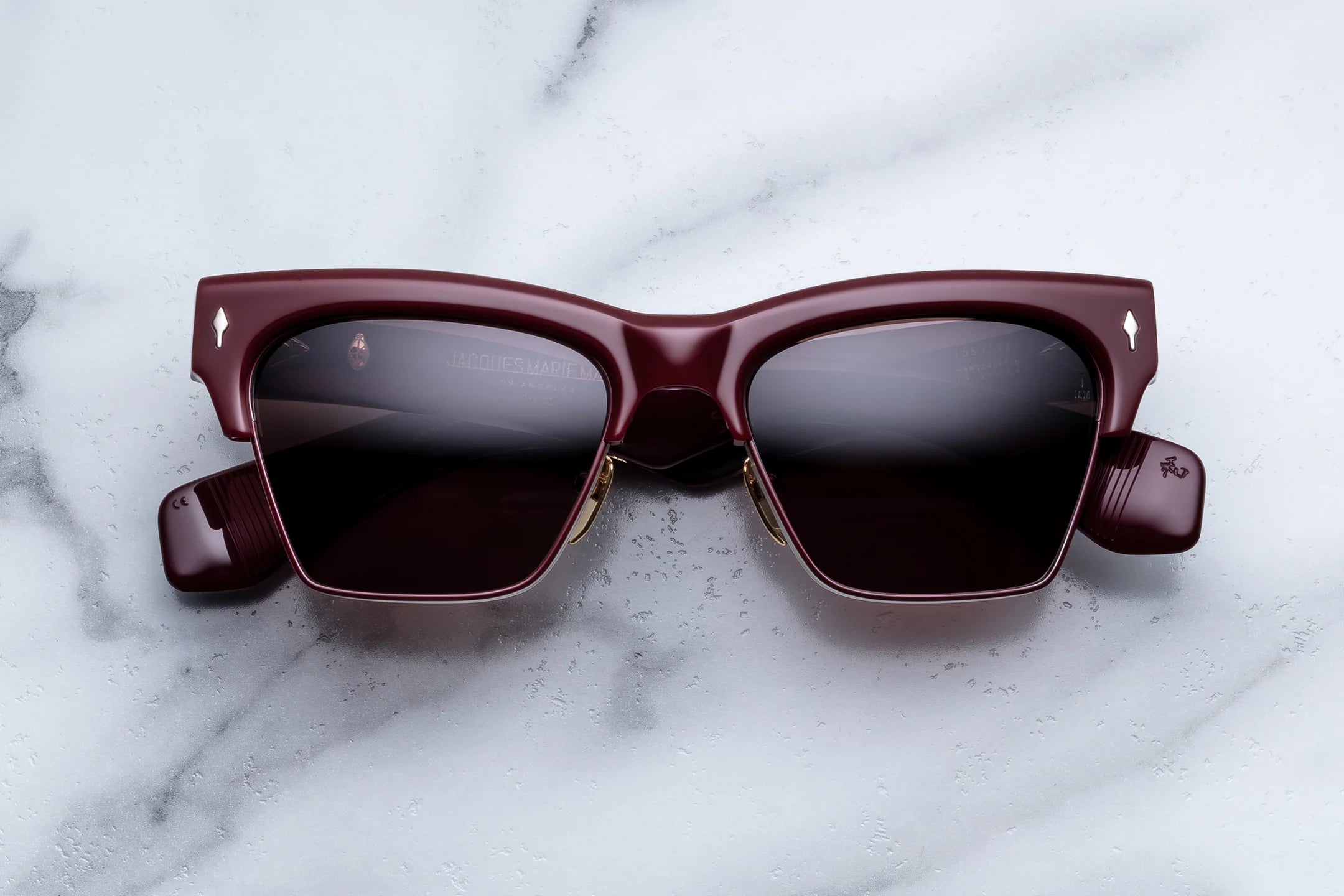 A pair of square-frame sunglasses with dark burgundy acetate frames and dark lenses, resting on a white marble surface.