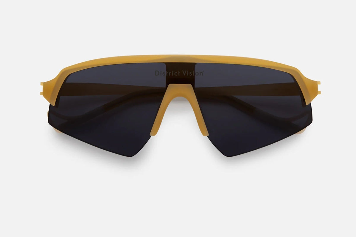 The District Vision Choji Turbo Blade features yellow frames and large, dark therapeutic grade lenses for enhanced eye protection during intense activity. The District Vision brand name is subtly displayed on the top of the lenses, and the sunglasses are shown against a plain white background.