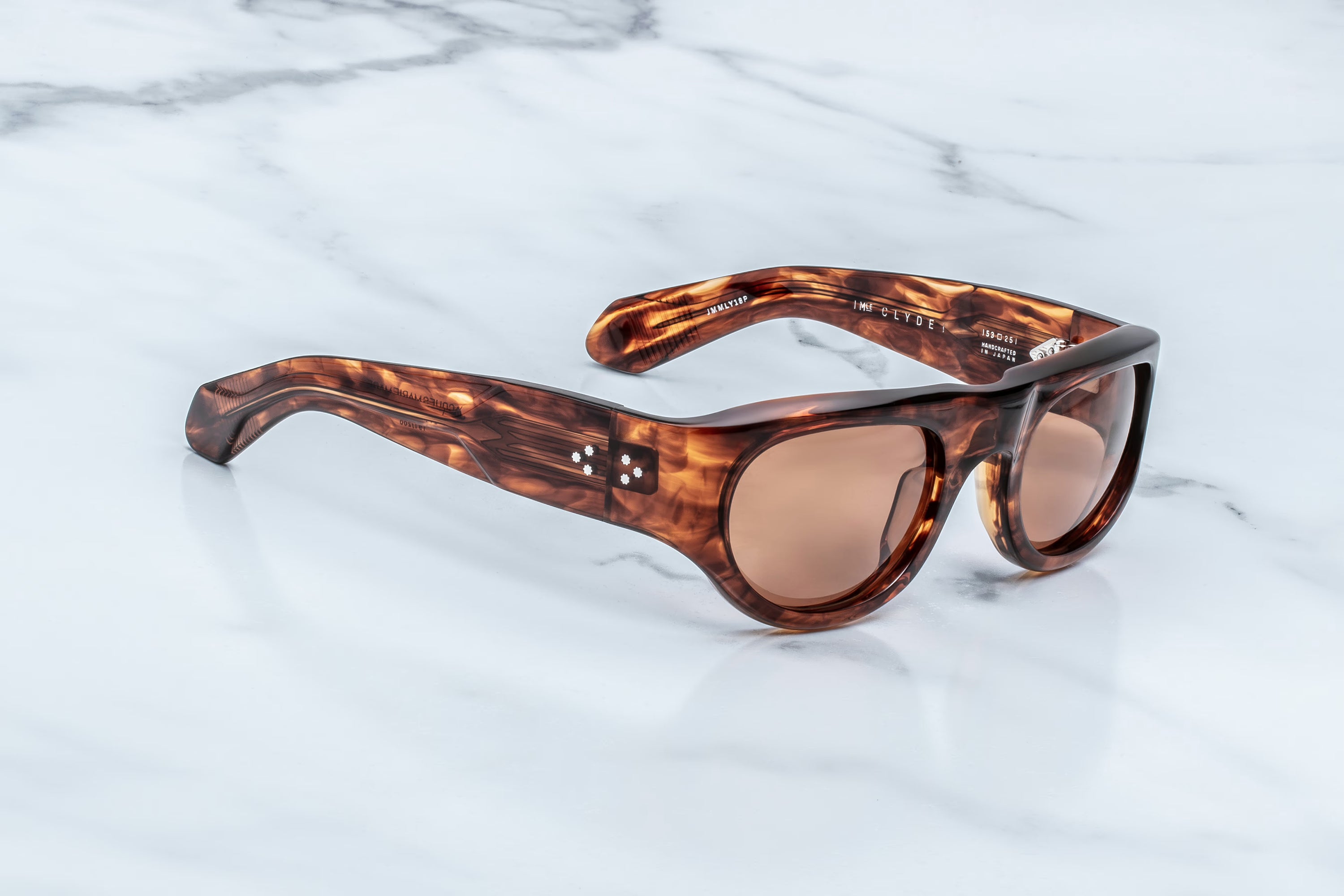 Jacques Marie Mage Clyde sunglasses by Jacques Marie Mage, featuring a distinctive tortoiseshell frame and brown-tinted lenses ideal for a carefree escape, rest elegantly on a white marble surface.