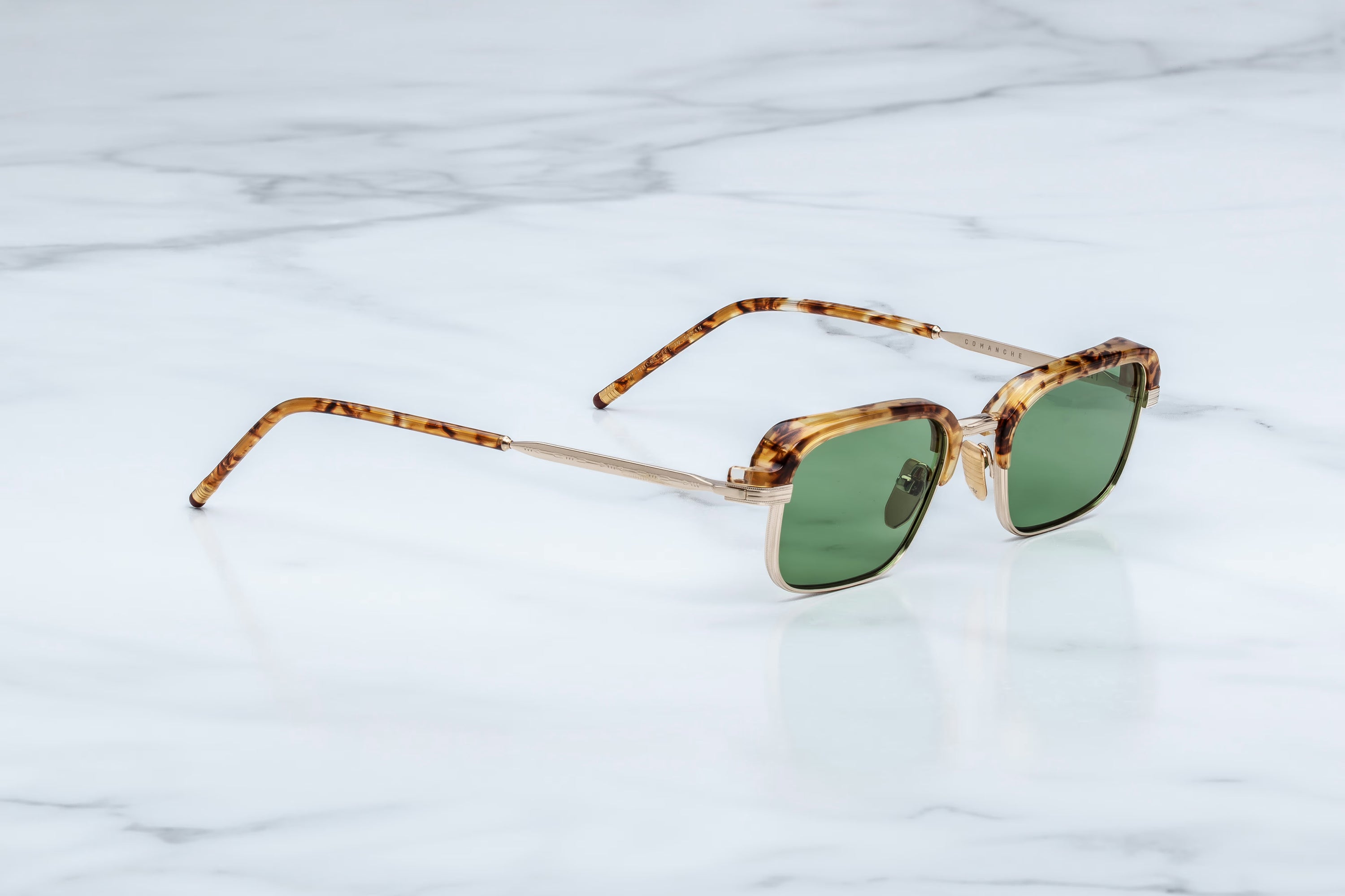 Sunglasses with tortoiseshell frame and green lenses on a marble surface