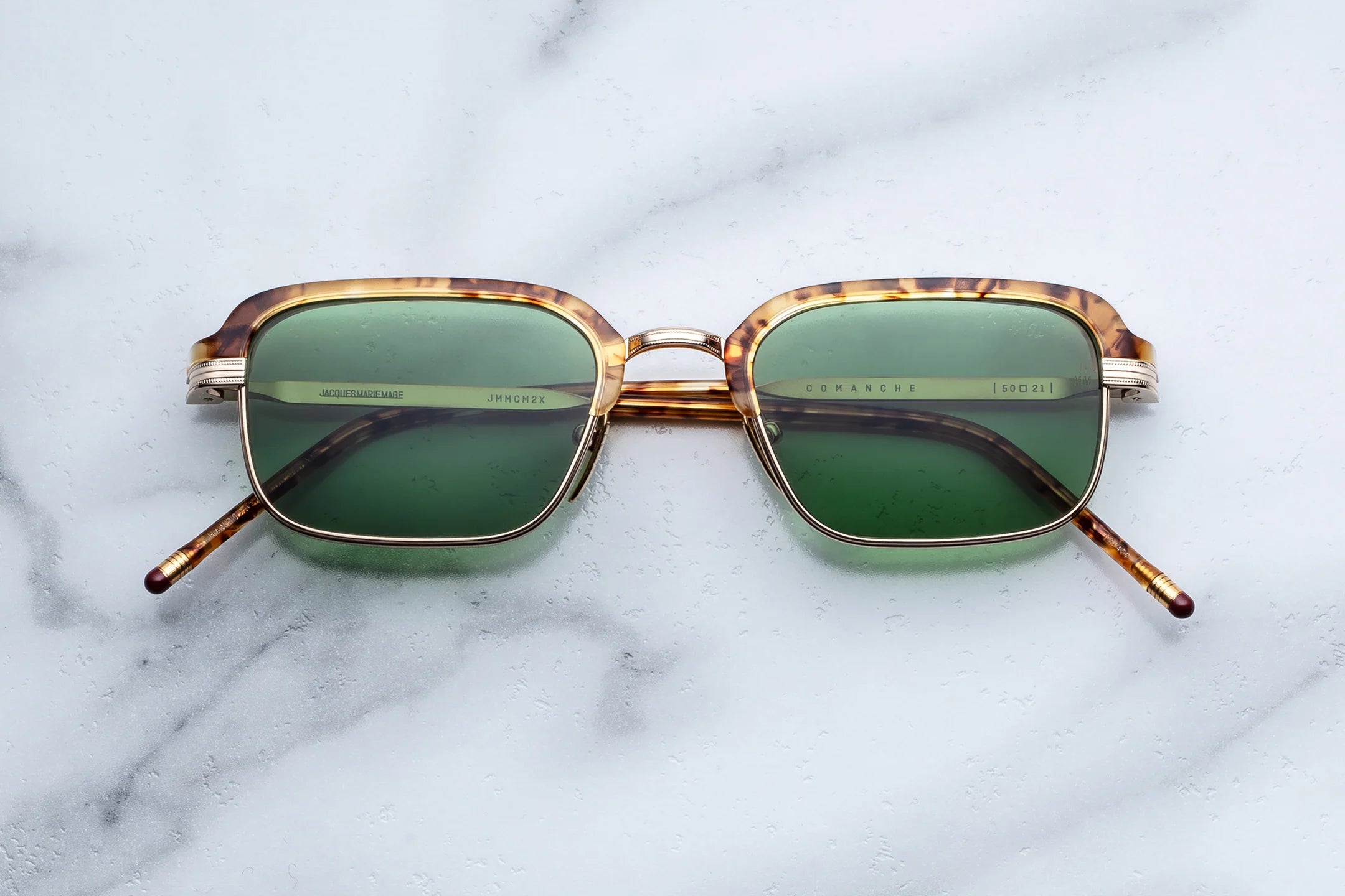 Sunglasses with green lenses and gold frames on a marble surface