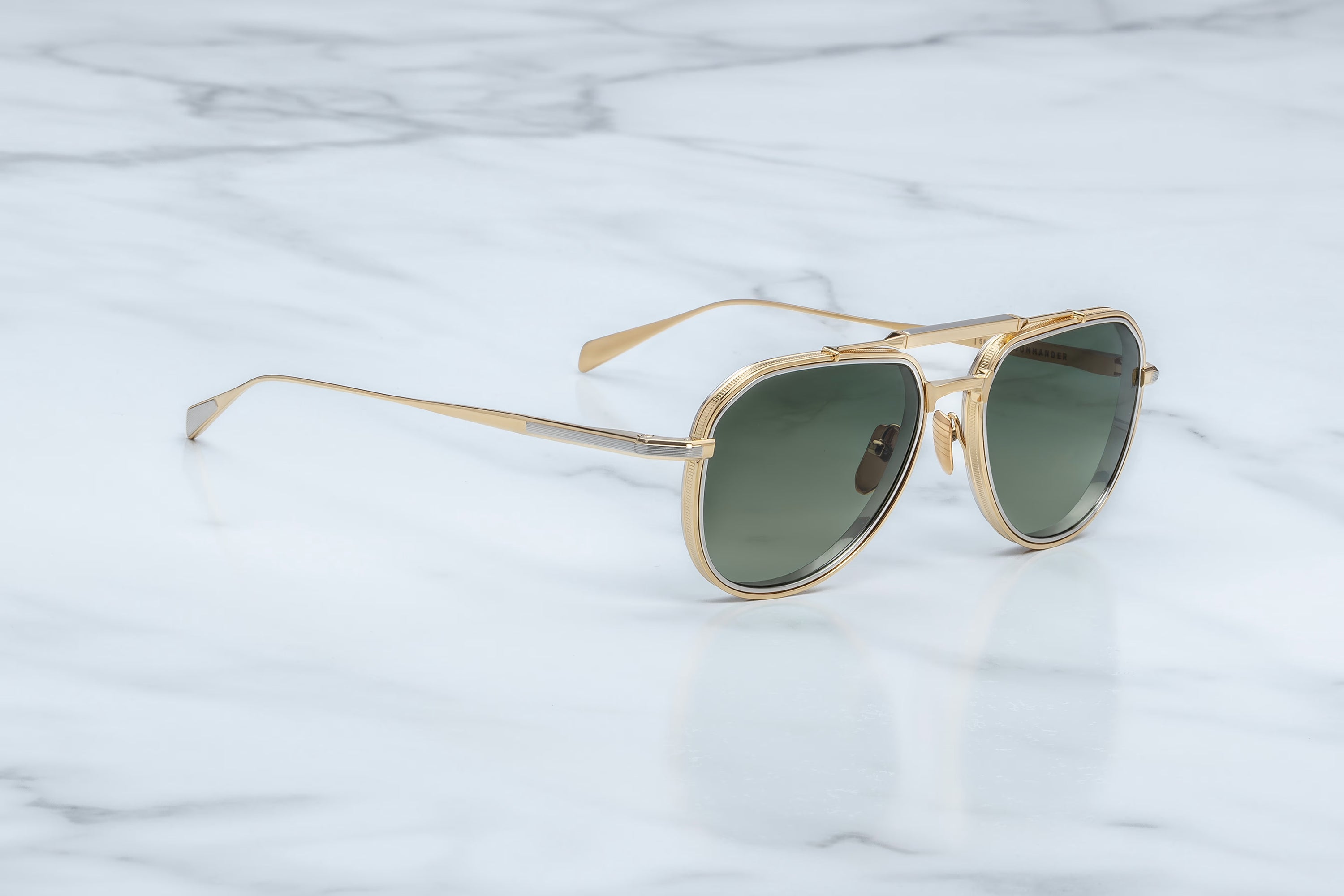 Gold-framed sunglasses with green lenses on a light marble background