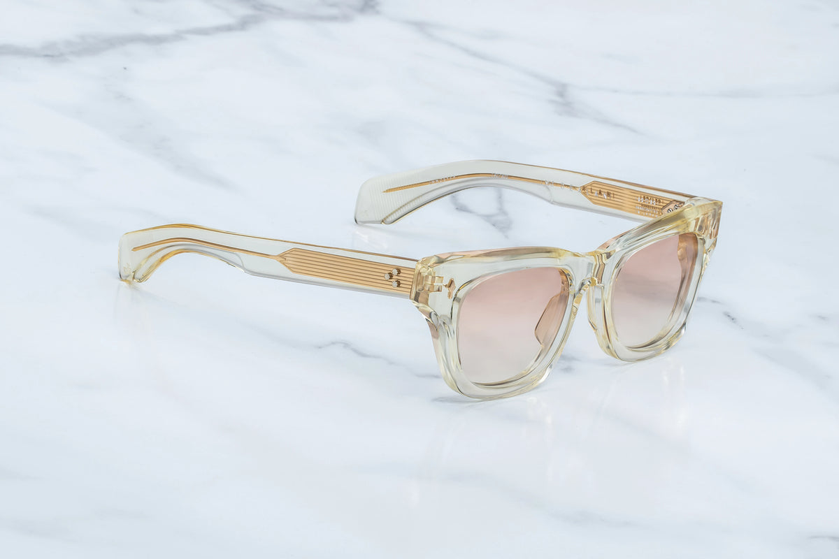 Jacques Marie Mage Dealan sunglasses featuring clear, translucent frames, pink-tinted custom photochromic lenses, and gold-toned metal detailing on the temples.