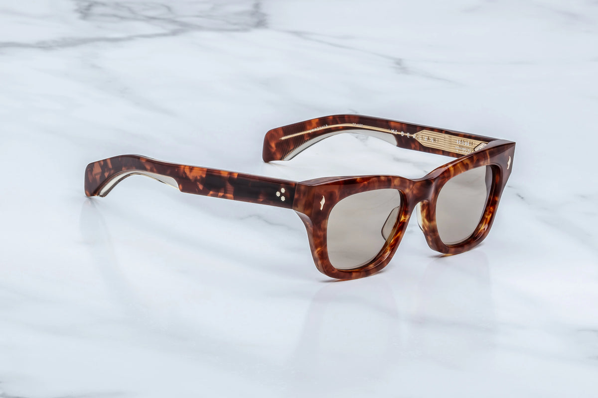 Tortoiseshell Jacques Marie Mage Dealan sunglasses with rectangular frames and gold-tone detailing on a white marble surface.