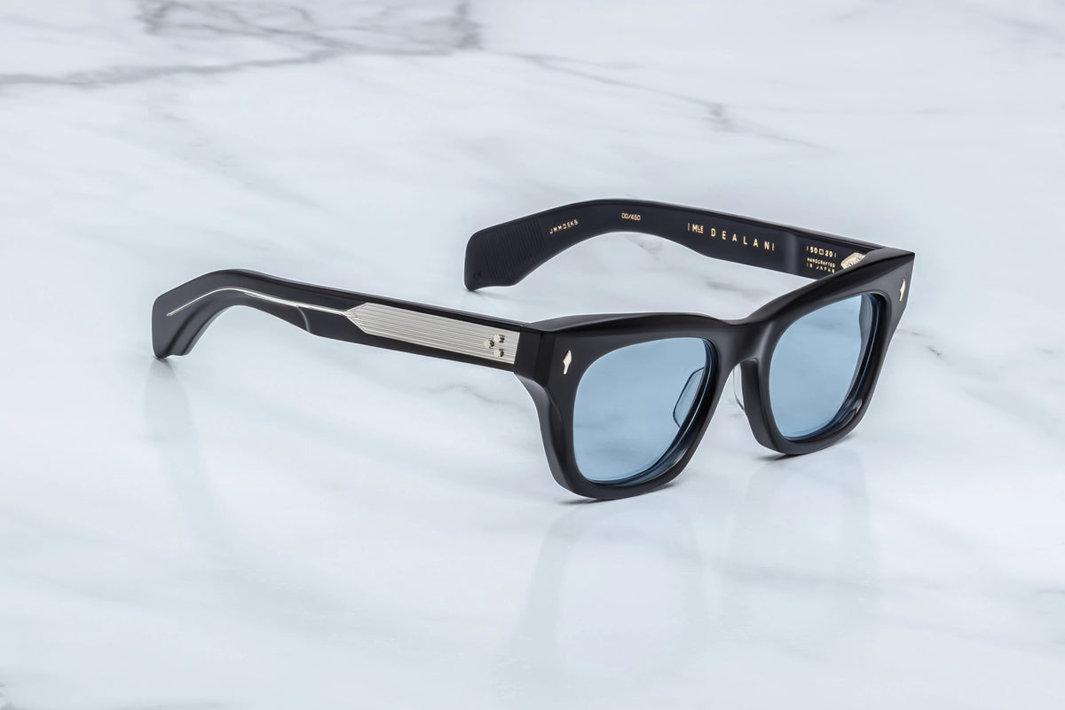 Jacques Marie Mage Dealan sunglasses featuring black frames, light blue lenses, and silver-toned metal detailing on the temples.