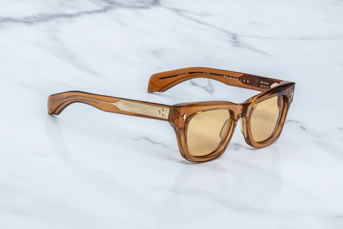 Jacques Marie Mage Dealan sunglasses featuring translucent brown rectangular frames, photochromic lenses for UV protection, and gold-tone metal detailing on the temples.