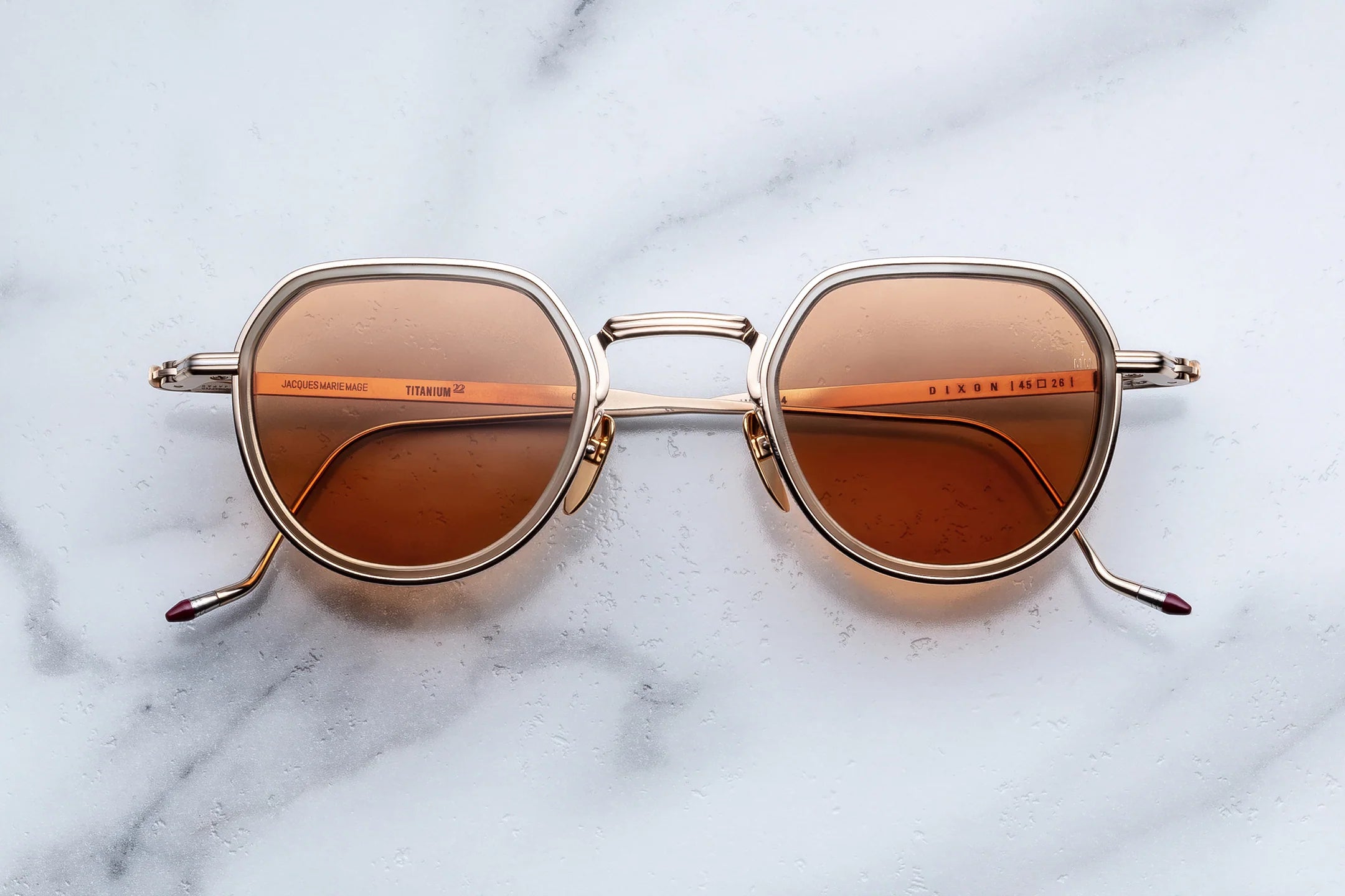 Sunglasses with brown lenses and gold frame on a marble surface