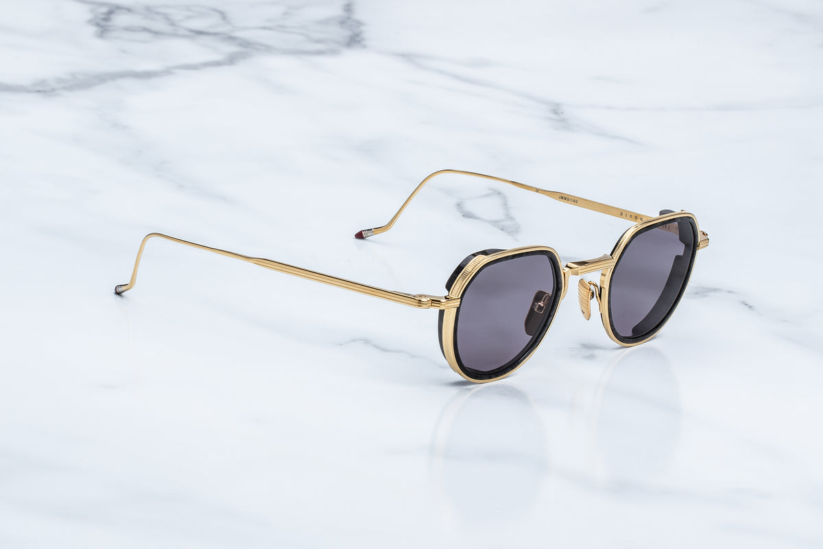 Gold-framed round sunglasses with dark gray lenses, resting on a white marble surface.