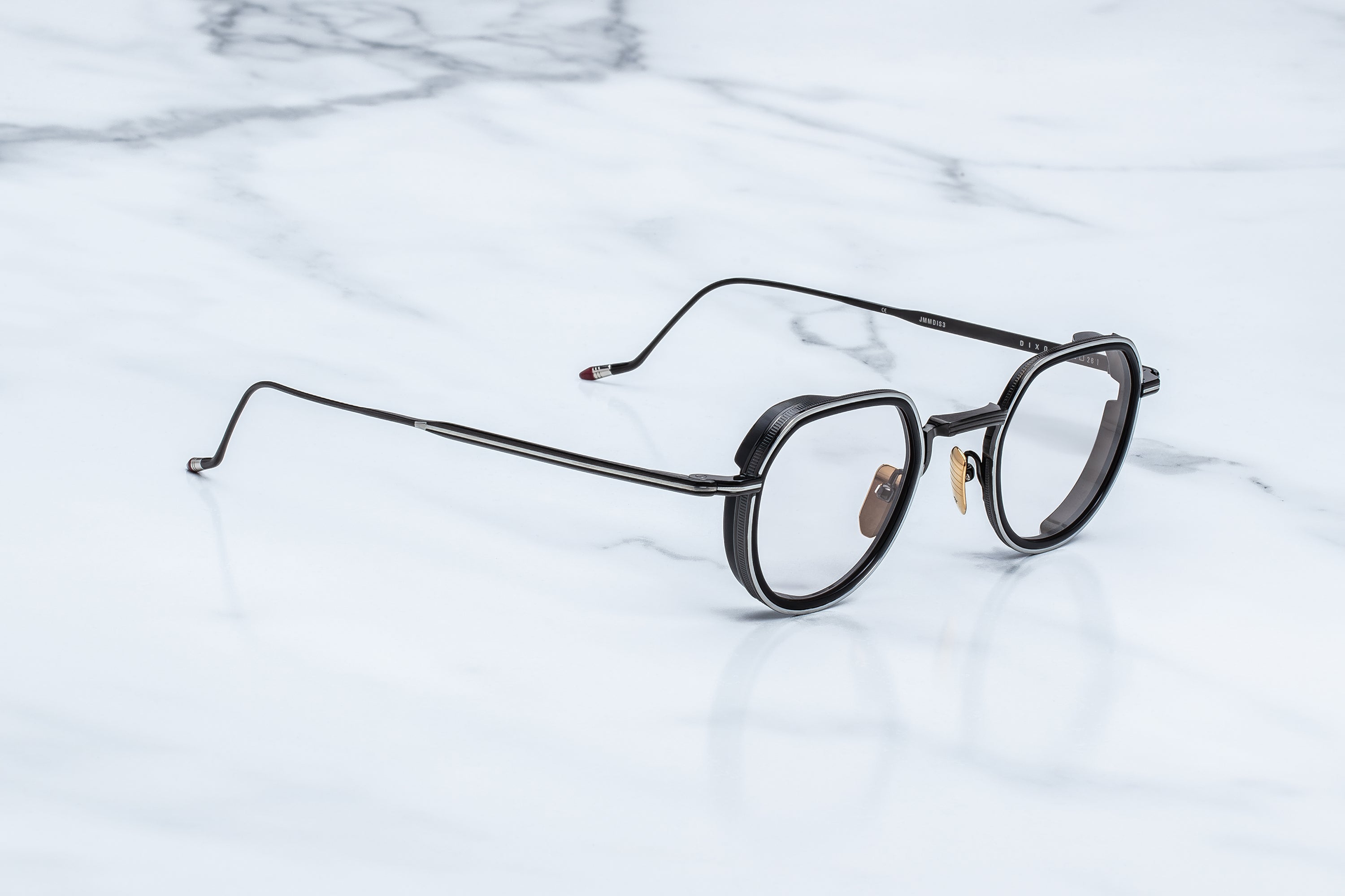 Jacques Marie Mage Dixon eyeglasses by Jacques Marie Mage—sleek black round frames with thin metal arms and clear lenses—resting on a white marble surface, embodying an understated accessory for rogue philosophers with an outlaw spirit.