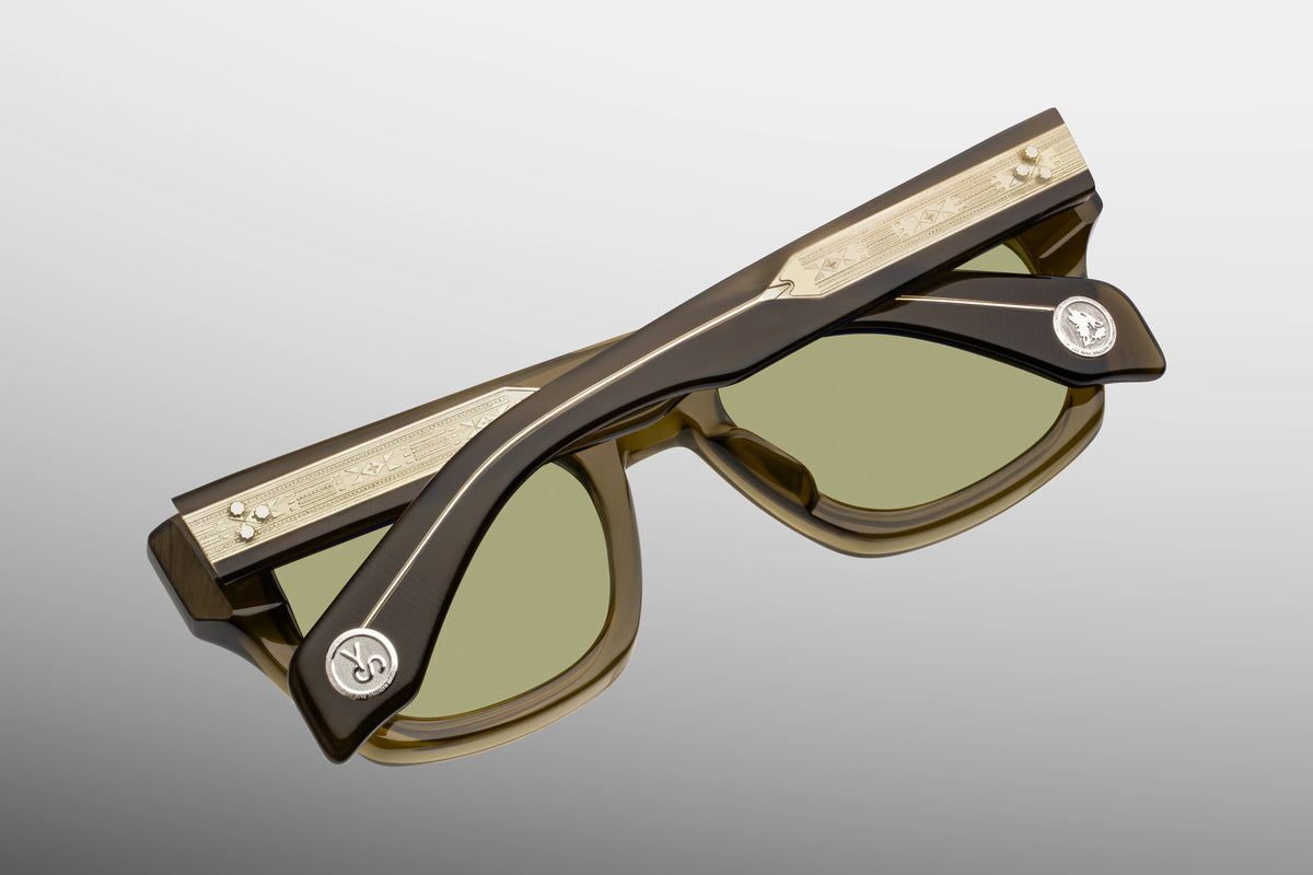 Jacques Marie Mage Yellowstone VII: Haynes In Green Moss spectacles, featuring ’60s-inspired thick, translucent olive frames and ornate gold-toned metal detailing along the temples.