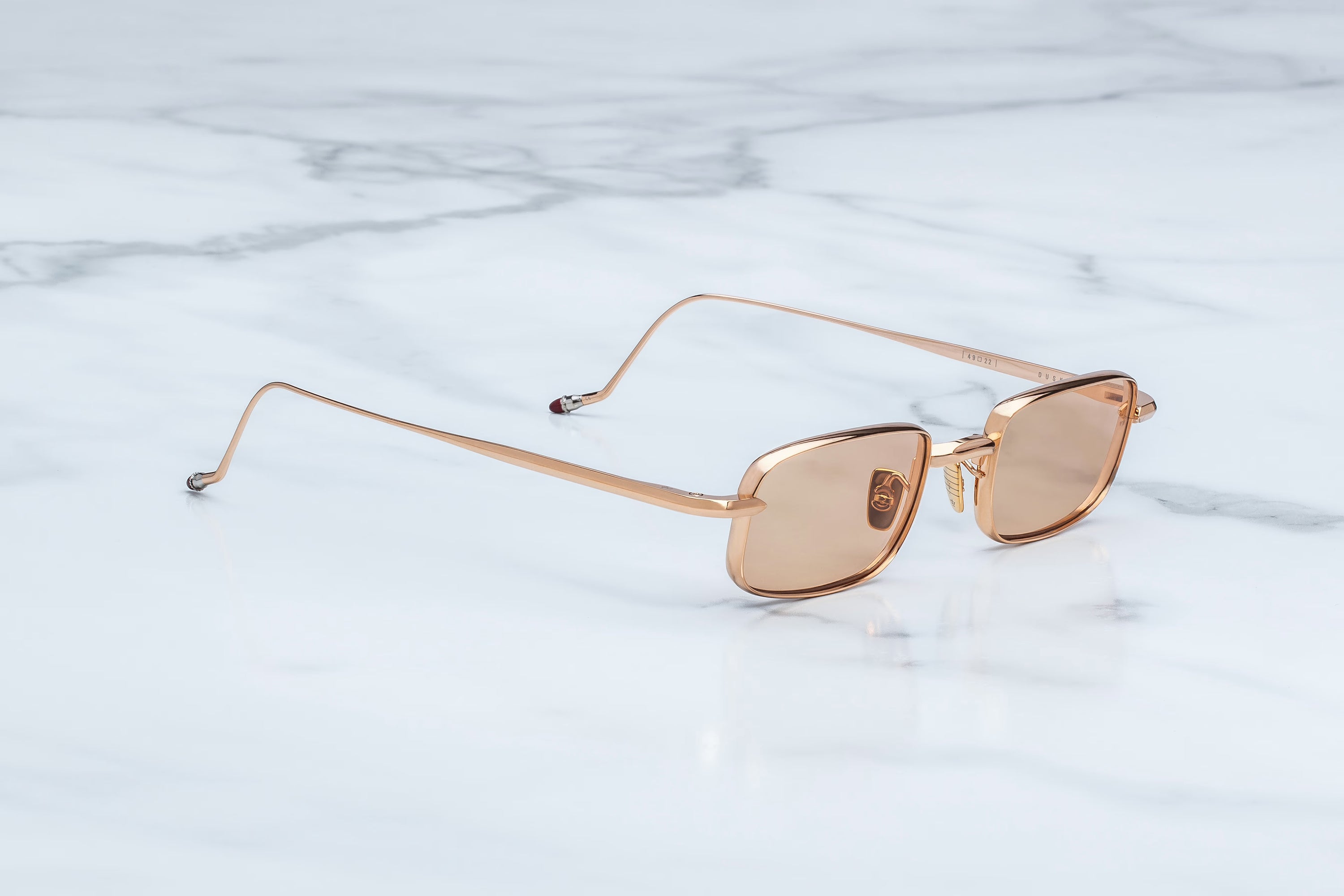 Oversized square sunglasses with a rose gold metal frame and translucent rose gold lenses, resting on a white marble surface.
