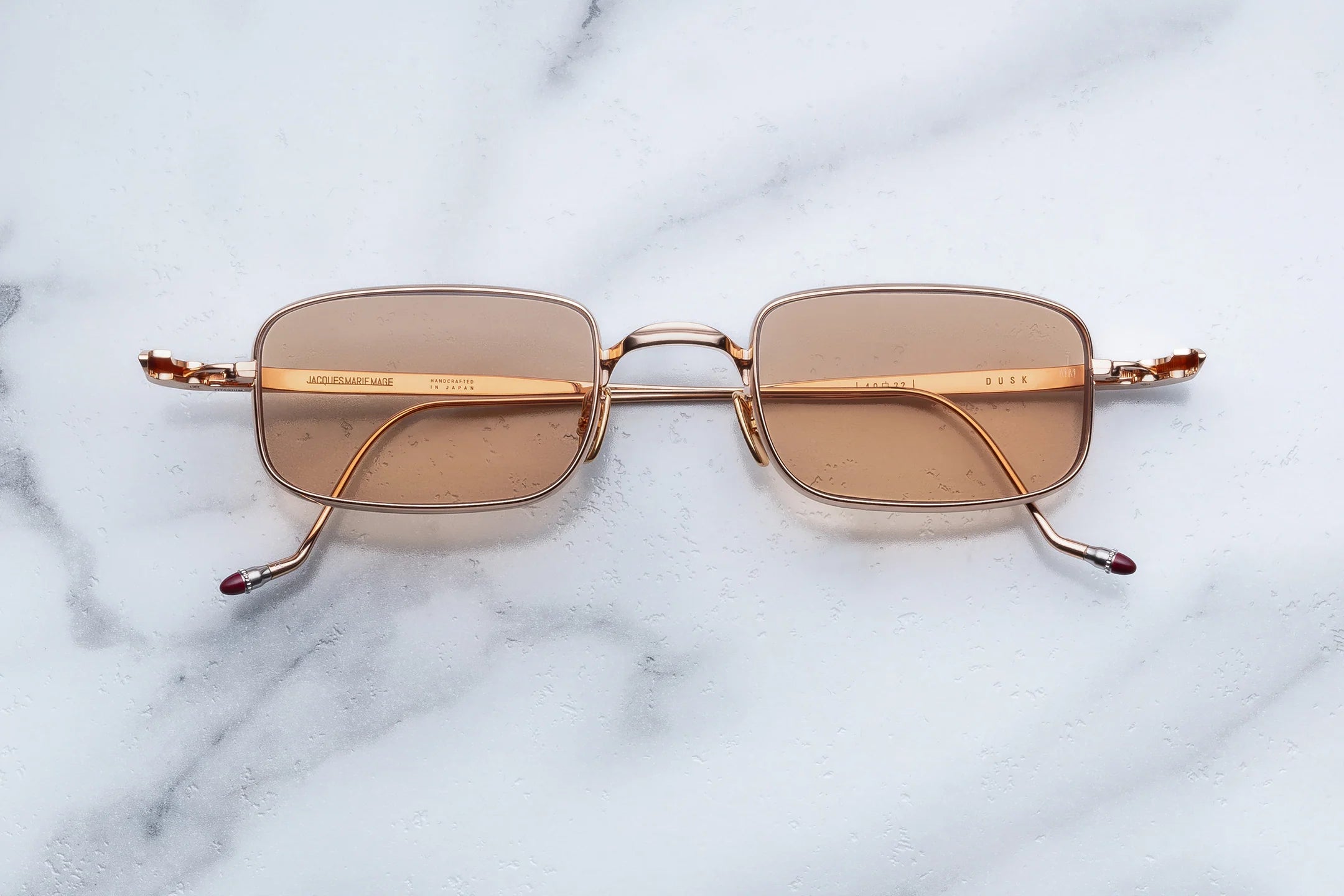 Sunglasses with gold frame and brown lenses on a marble surface