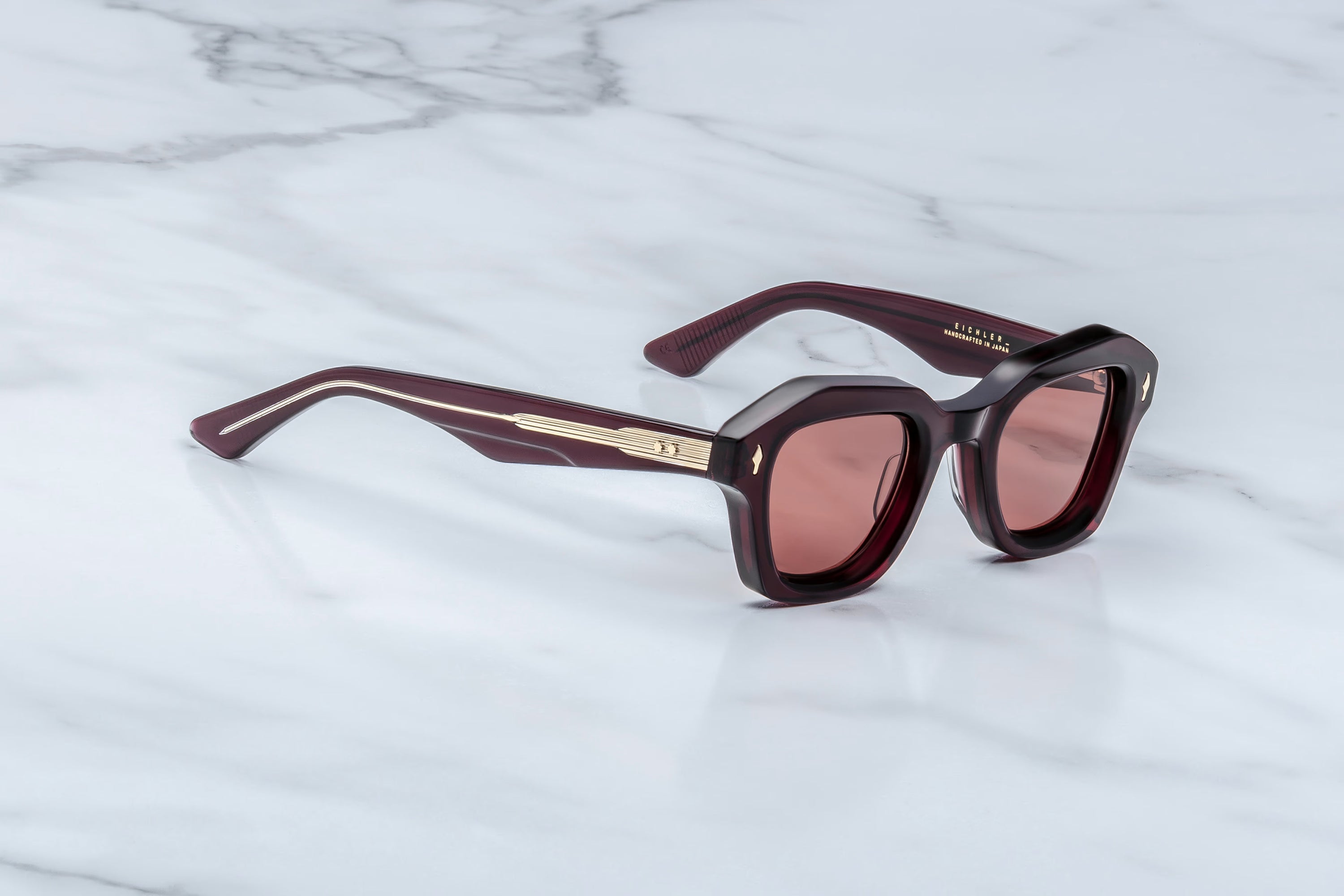 Sunglasses with a maroon frame and pink lenses on a marble surface