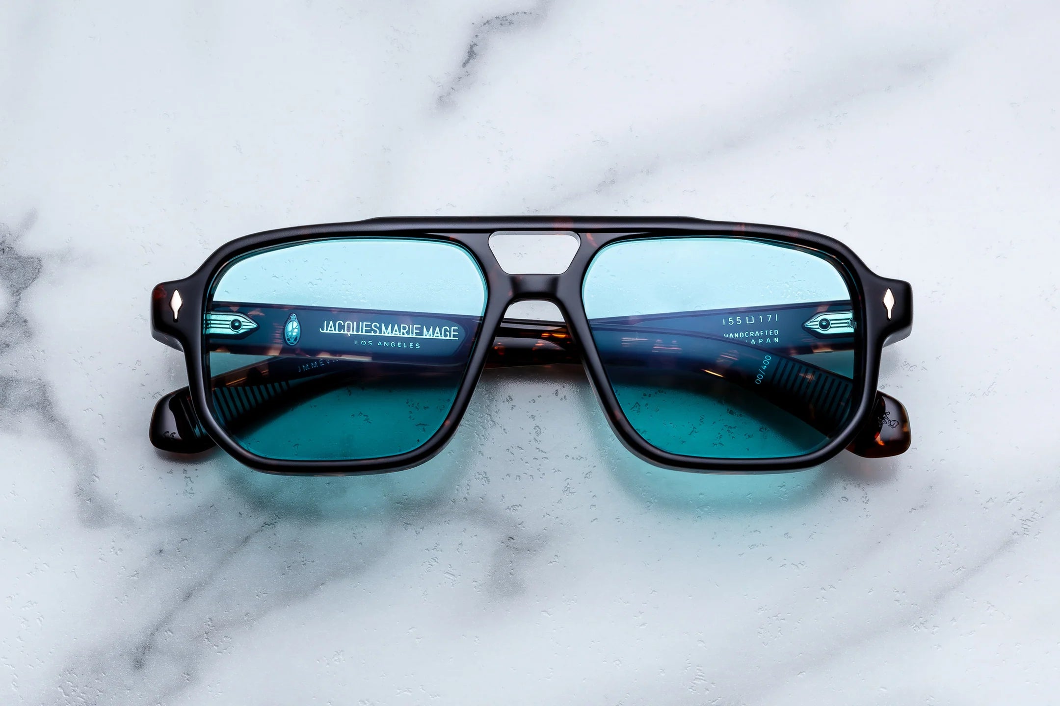 A pair of Oakley square sunglasses with a black frame and blue-tinted lenses, resting on a white marble surface.