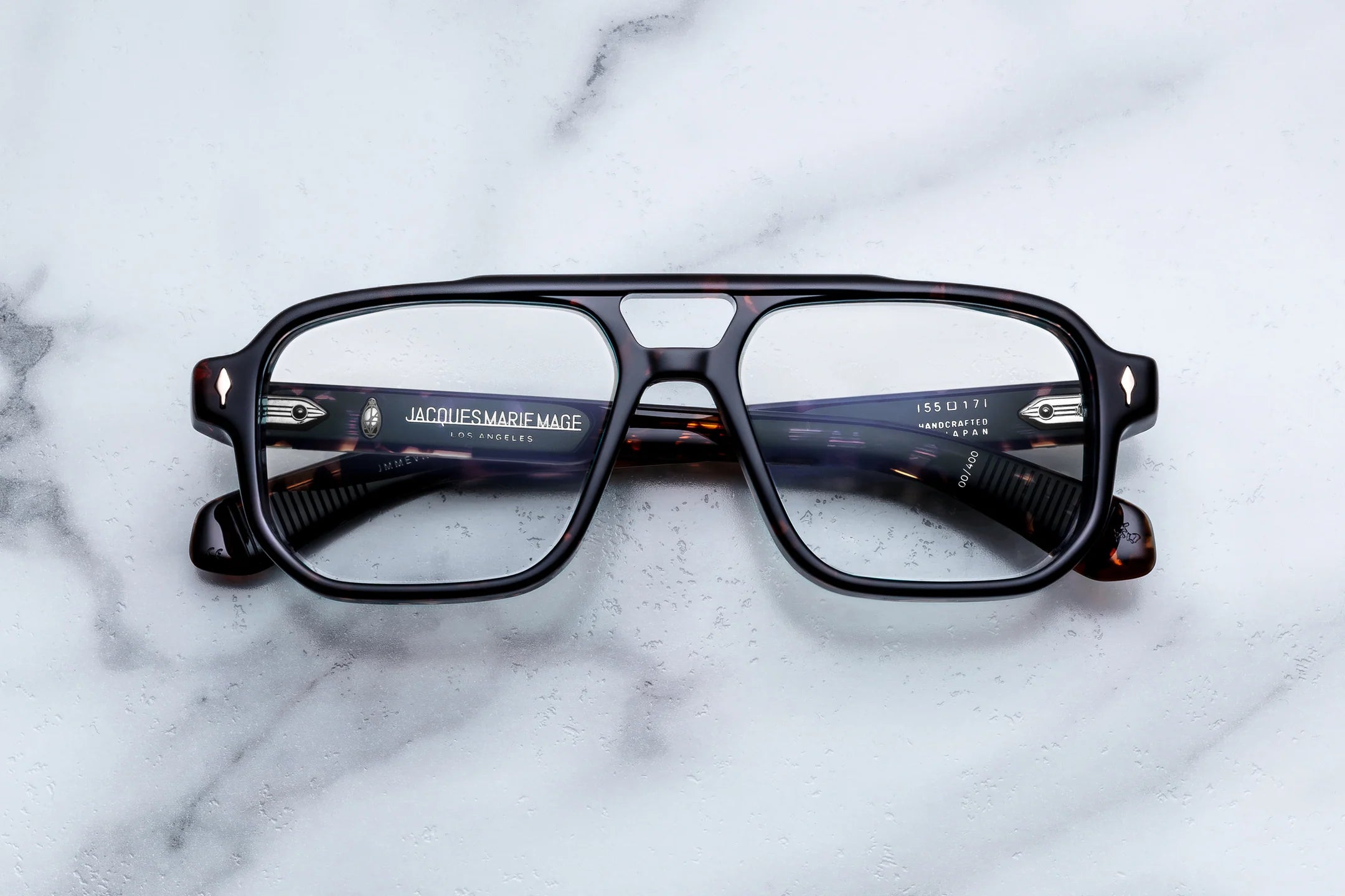 A pair of square-frame eyeglasses with a glossy black front and tortoiseshell temples, resting on a white marble surface. 