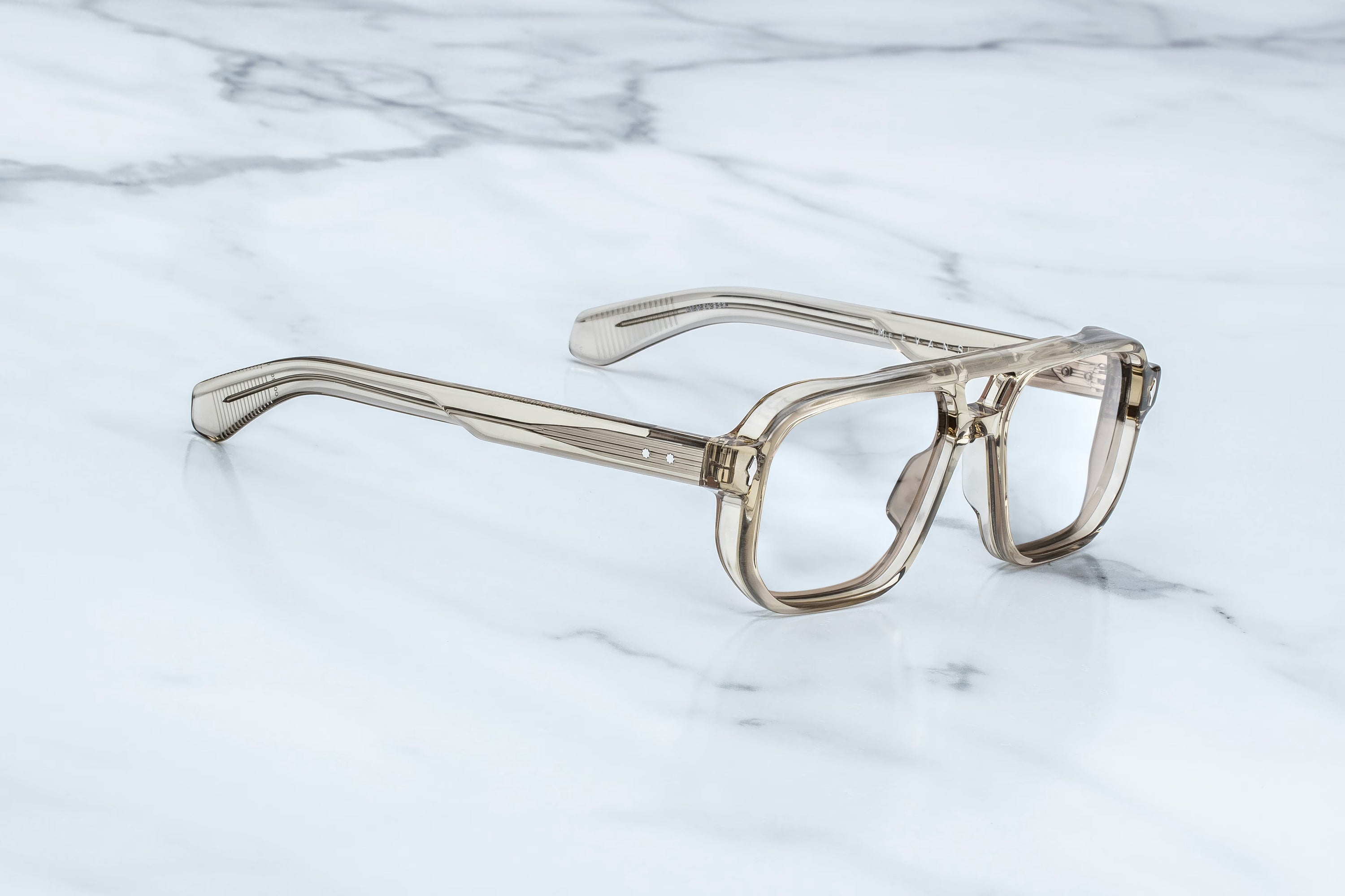 A pair of translucent smoky-tinted eyeglass frames with clear lenses, resting on a white marble surface with gray veining.