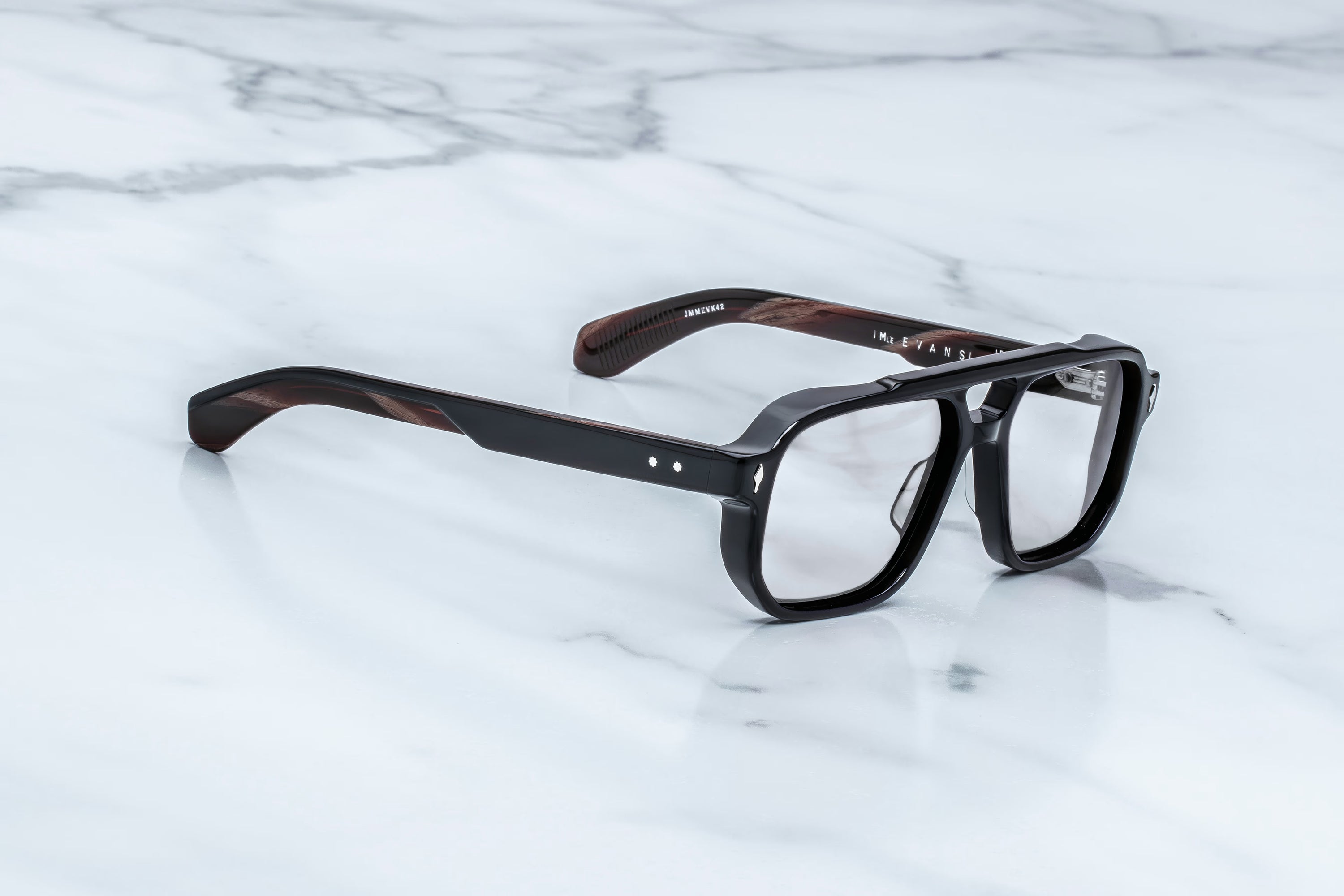 A pair of square-frame eyeglasses with a glossy black front and dark brown marbled temples, resting on a white marble surface.