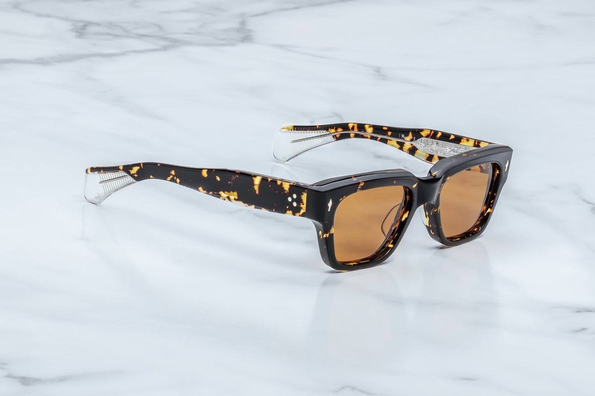 Jacques Marie Mage Fellini sunglasses by Jacques Marie Mage, featuring thick square frames in a tortoiseshell pattern and brown lenses, rest elegantly on a white marble surface.