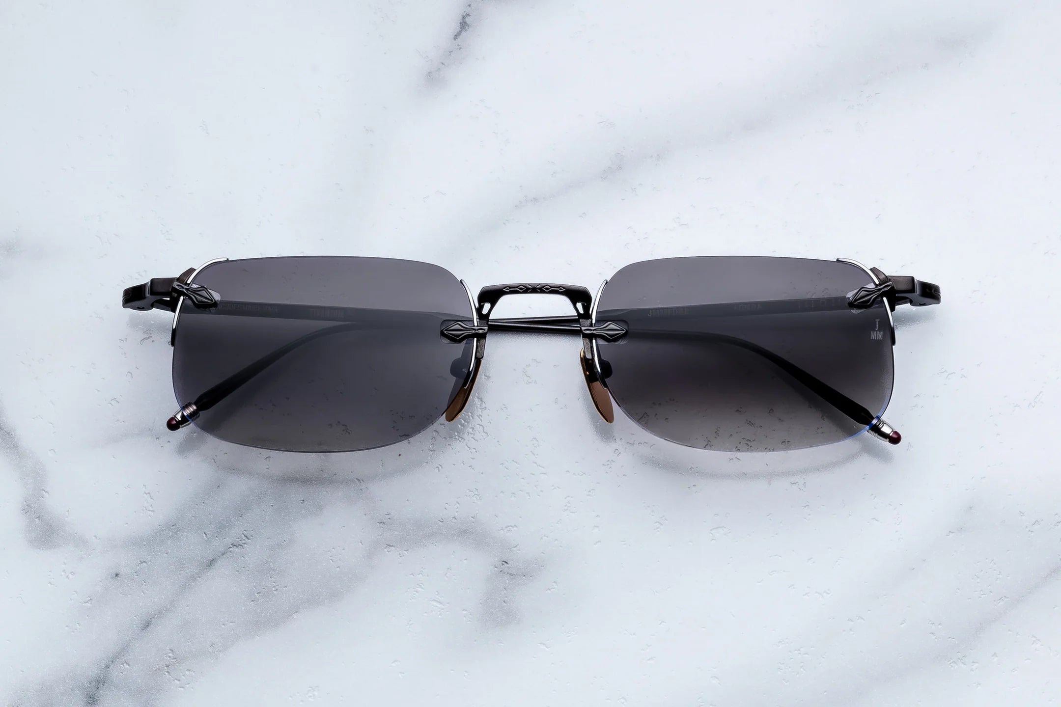 Rimless sunglasses with dark gray lenses and a thin black metal frame, displayed on a white marble surface.